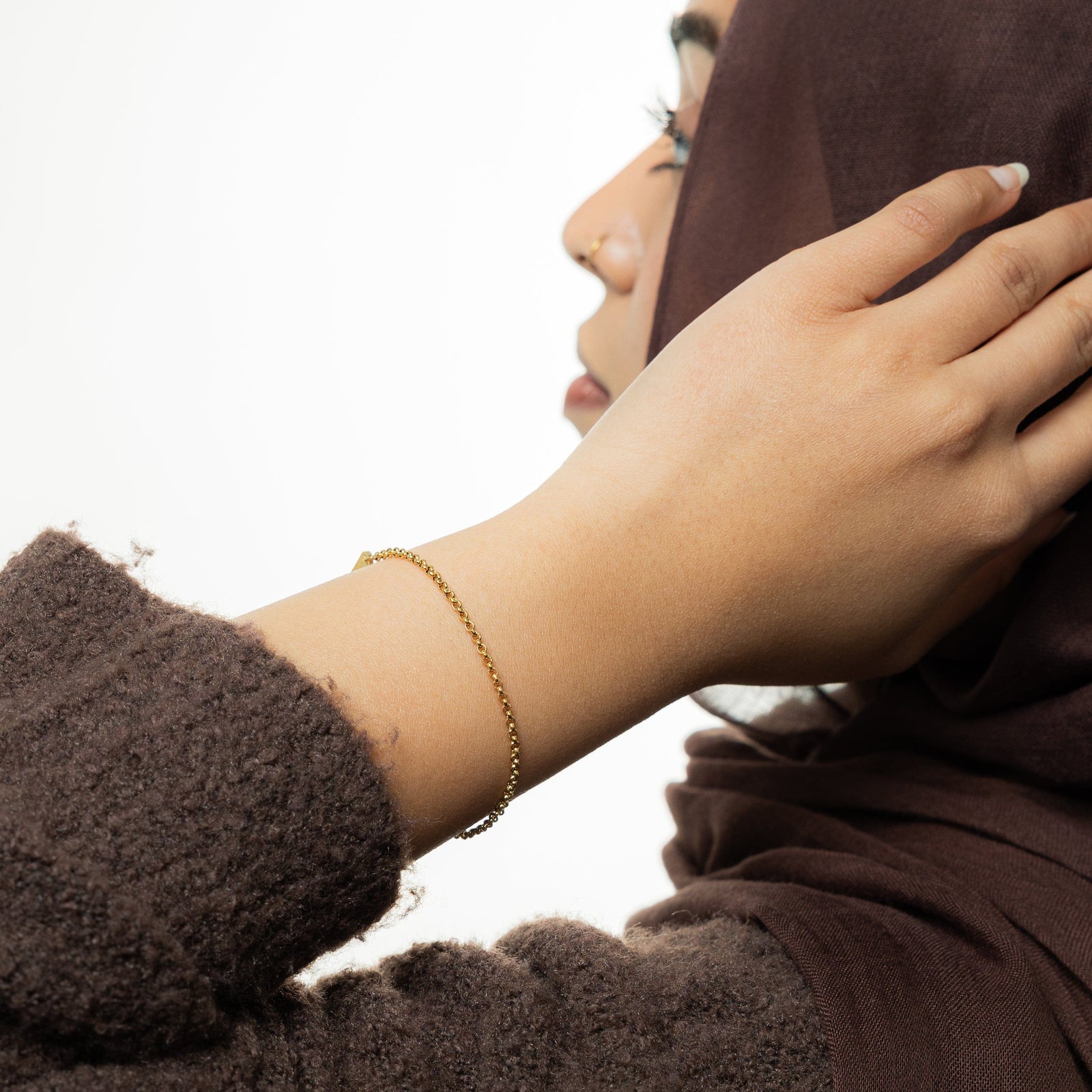 Photo of the model touching their hijab with their left hand, the model is also wearing the gold Micro Box Bracelet with their left hand.