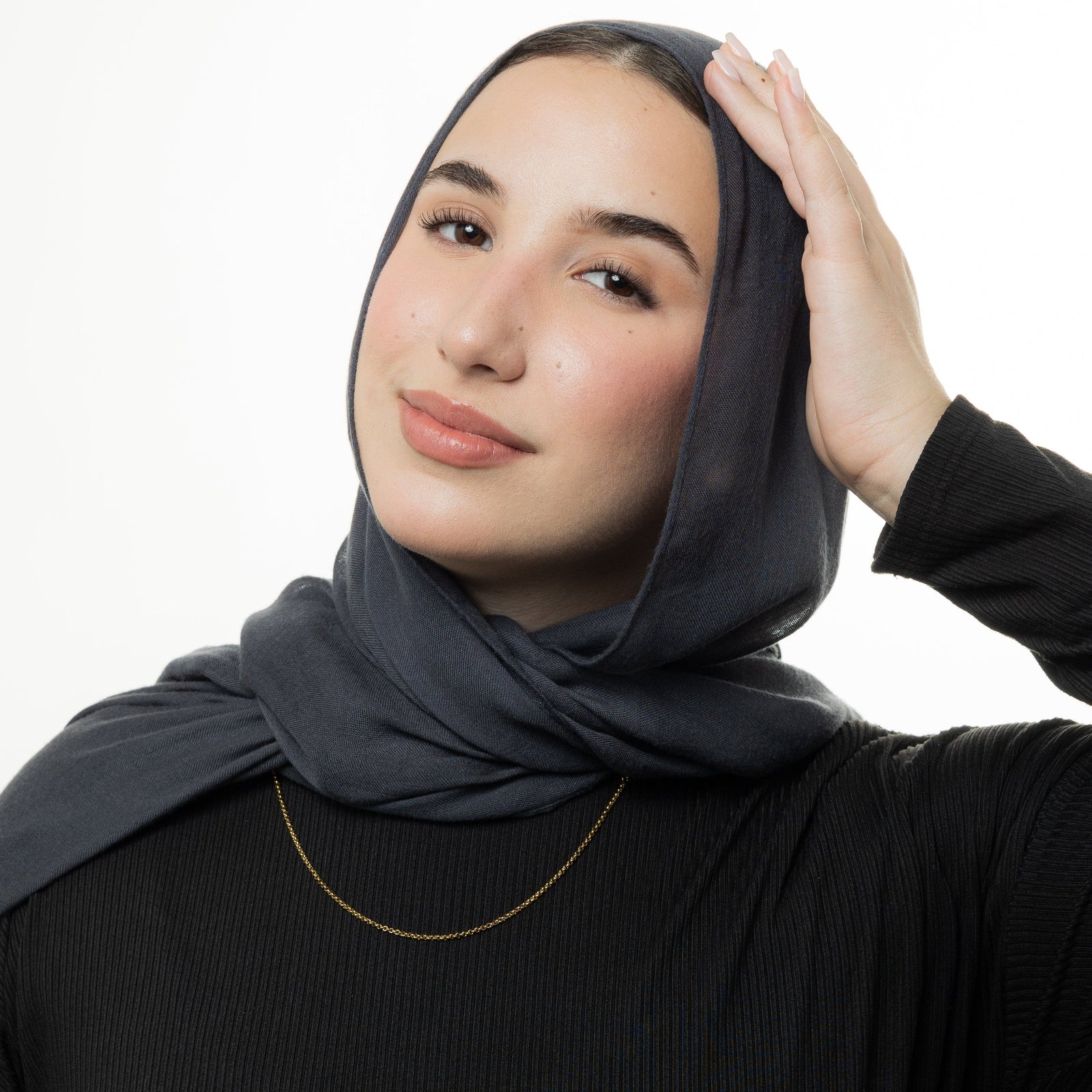 Photo of the model looking and smiling to the camera and resting their left hand on the top of their head. The model is wearing the gold Micro Box Chain.