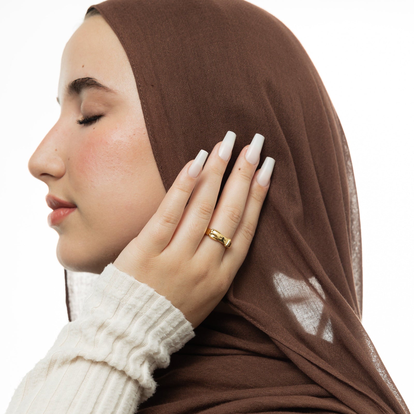Woman wearing a cream top, brown hijab, and a gold buckle ring