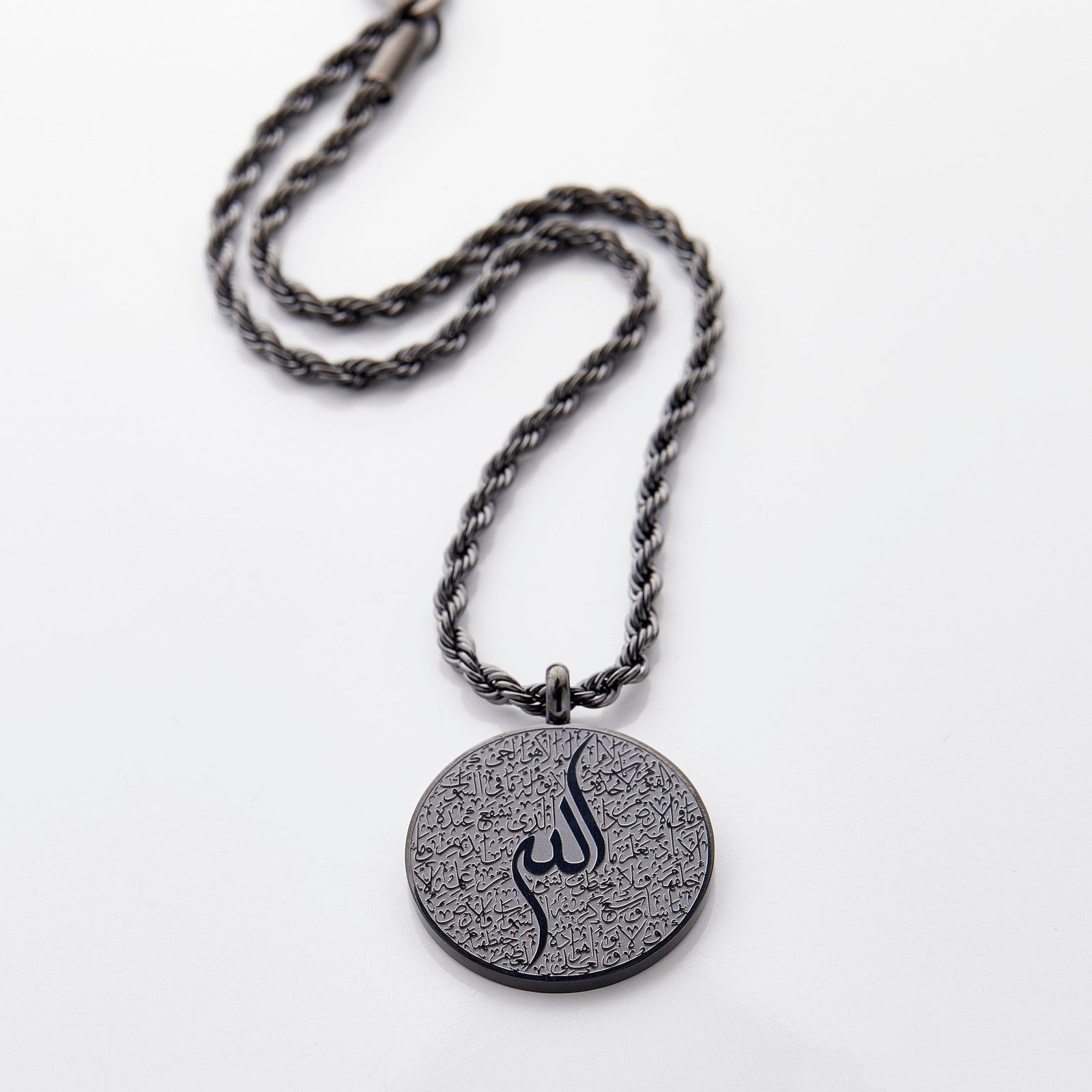 Black car hanger with a circular pendant engraved in Arabic calligraphy of Ayatul Kursi, styled flat on a neutral background.