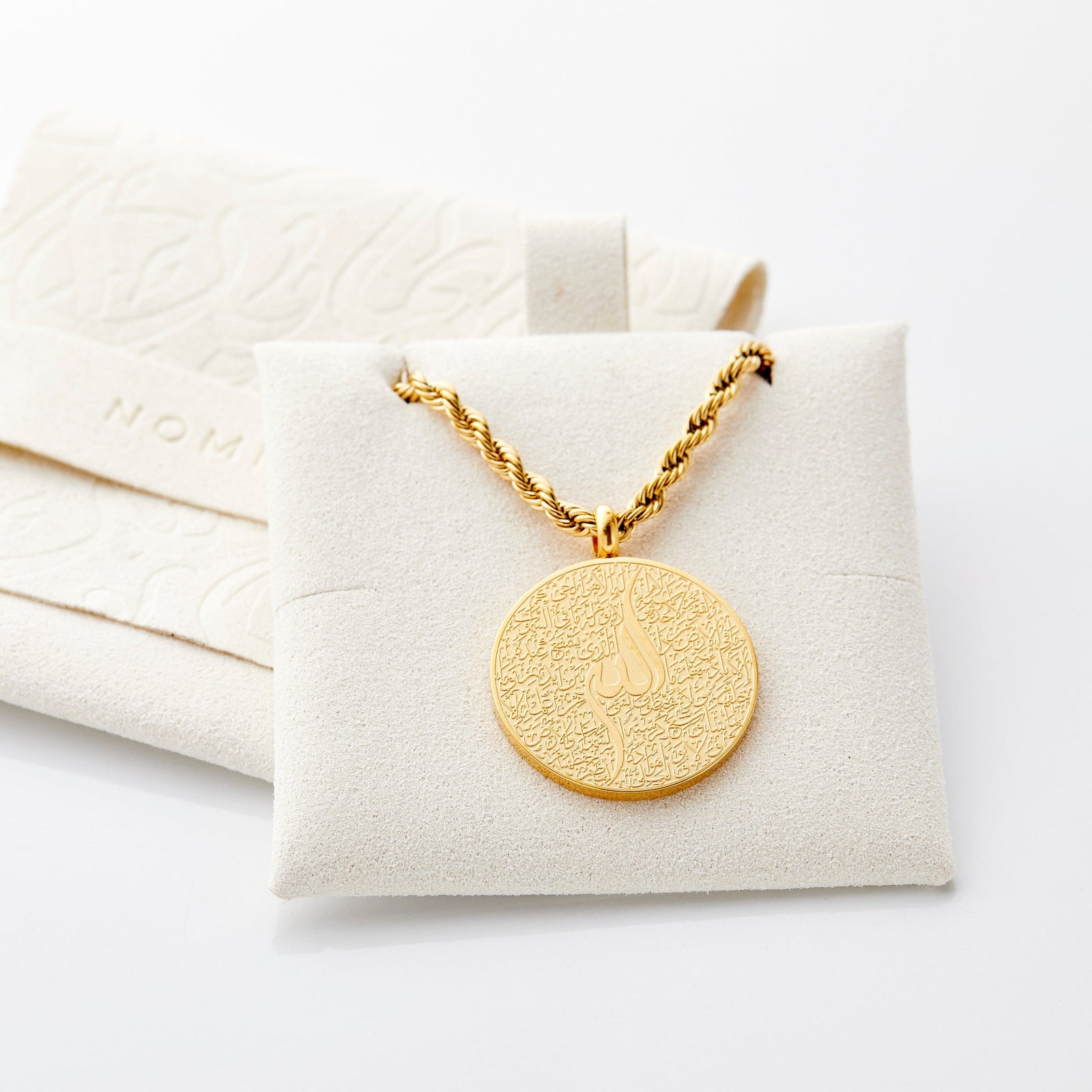 Gold Ayatul Kursi car hanger displayed on a beige Nominal jewelry pouch.