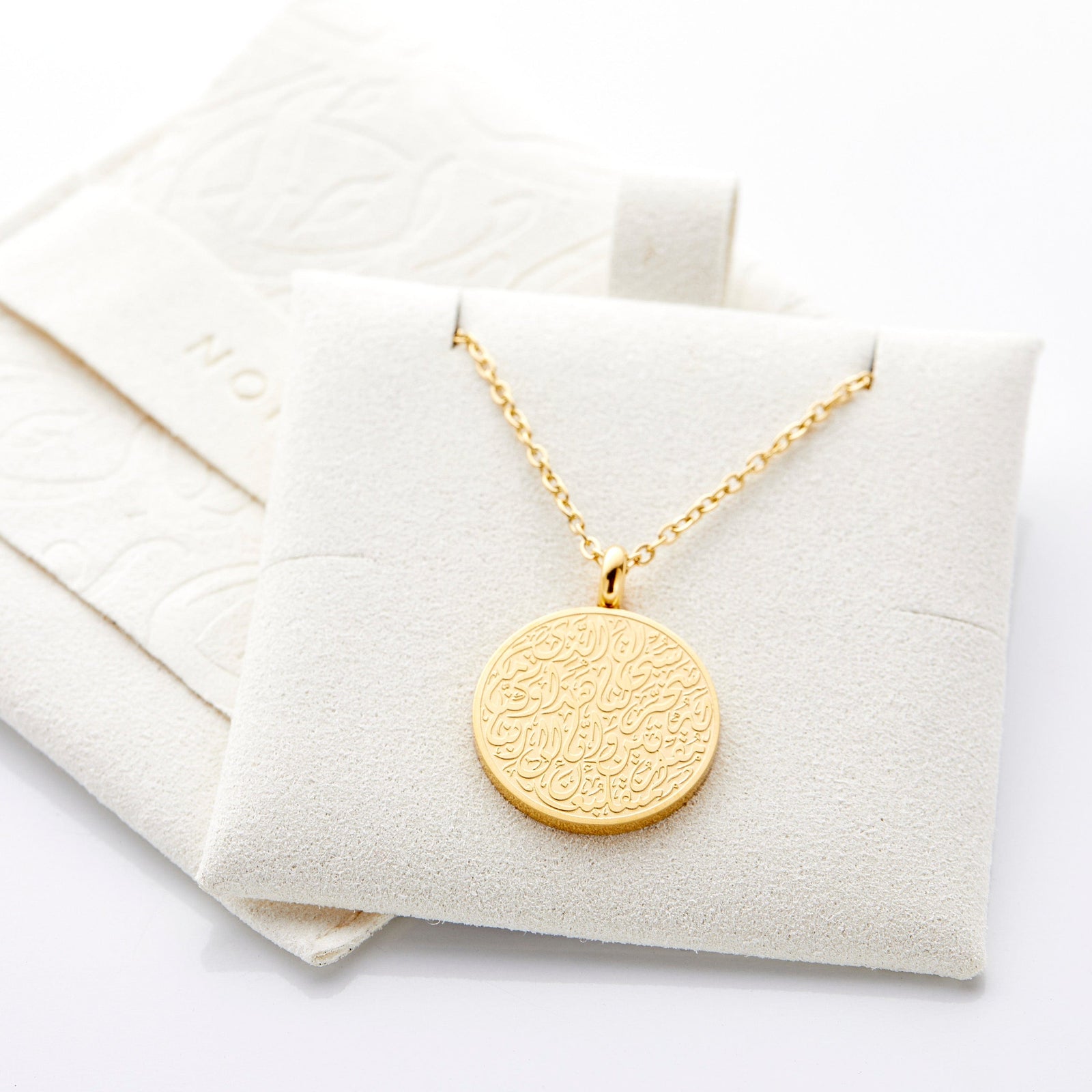 Gold Duaa Al-Safar pendant resting on cream Nominal pouch.