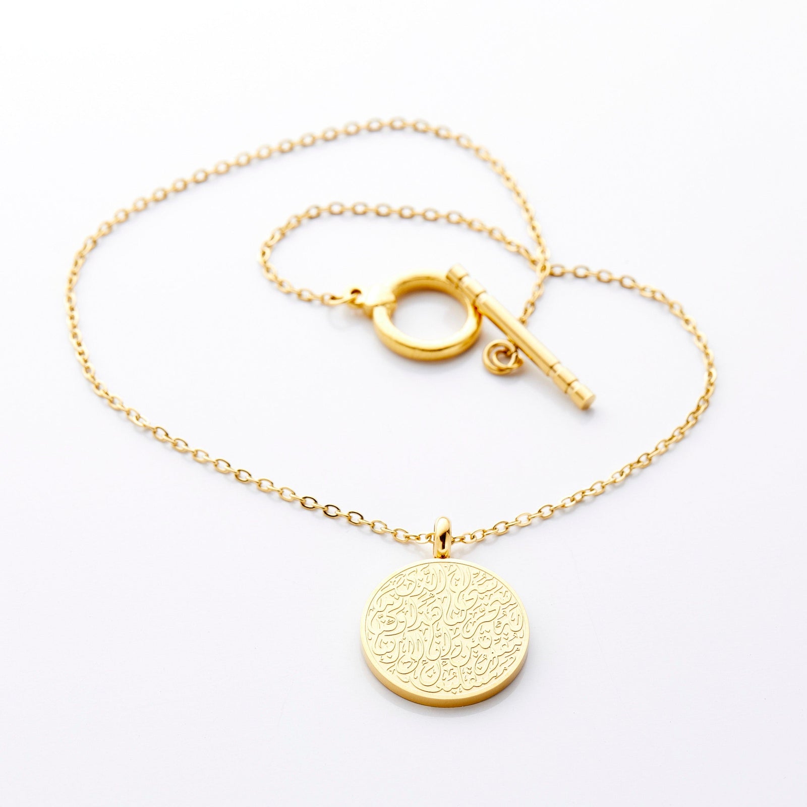 Gold circular pendant engraved with Arabic Duaa Al-Safar calligraphy on a fine chain, laid flat with toggle clasp visible against neutral background.