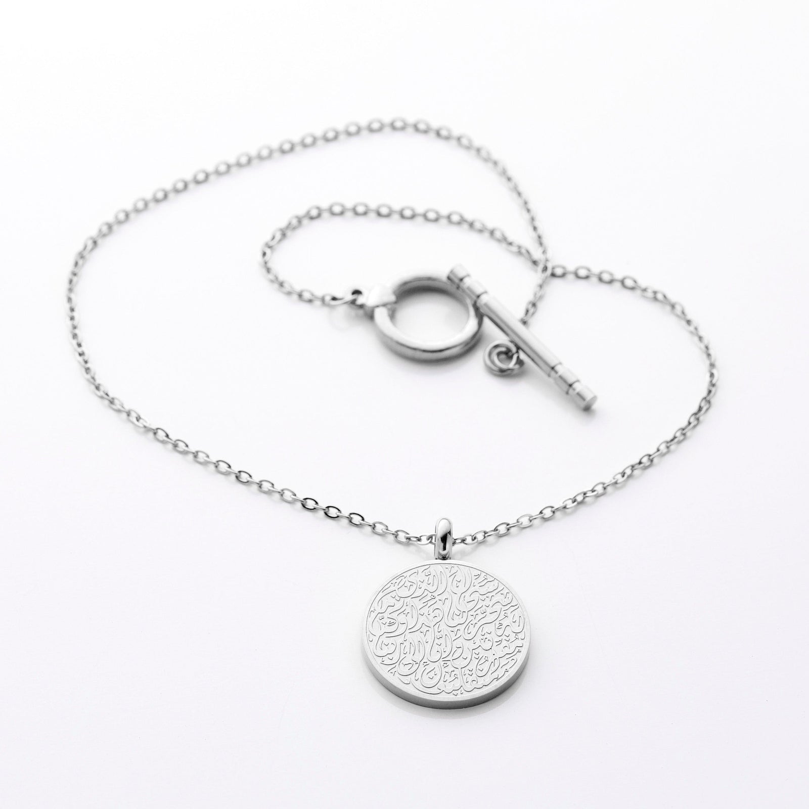 Silver circular pendant engraved with Arabic Duaa Al-Safar calligraphy, laid flat with toggle clasp visible against neutral background.
