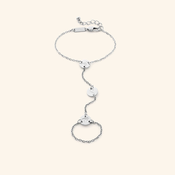 A delicate silver-plated hand chain bracelet featuring a chain that connects a bracelet around the wrist to a ring around a finger, with three small, round charms with intricate cut-out designs along the connecting chain. The hand chain is displayed against a light background.