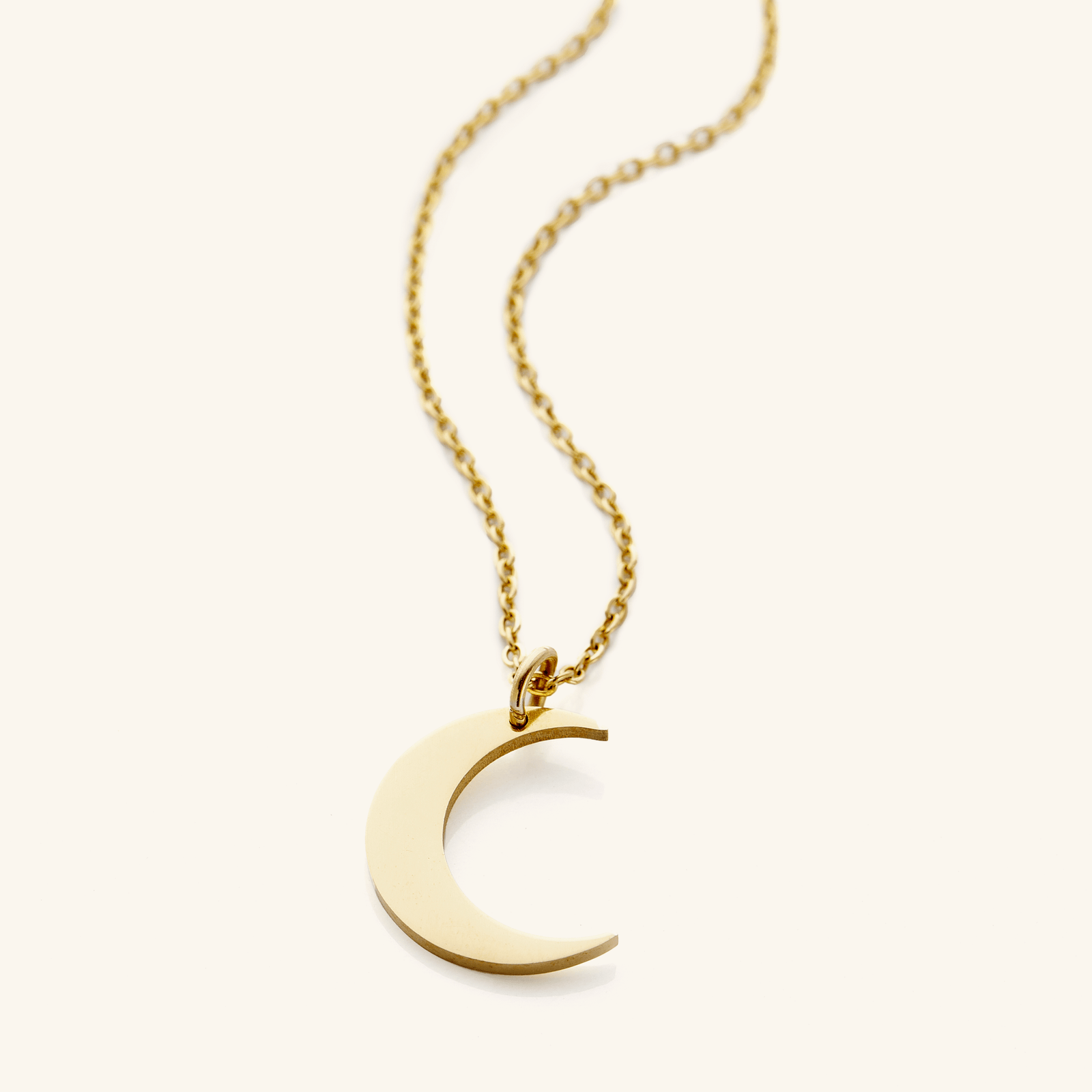 Flat lay of an 18k gold plated minimalist necklace that features a crescent pendant against a light background.