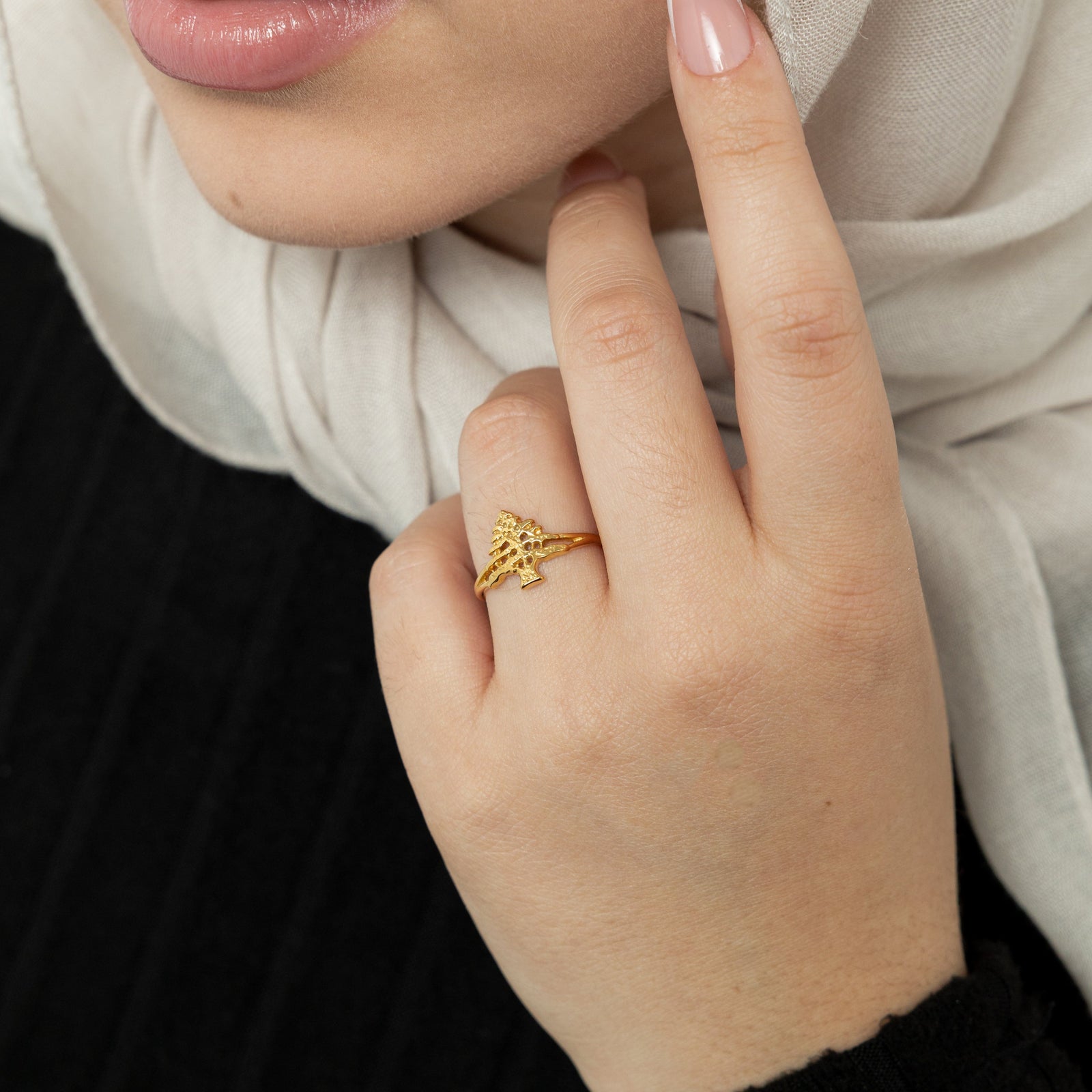 Woman wearing a gold Cedar of Lebanon ring on her finger, with the textured tree design visible.