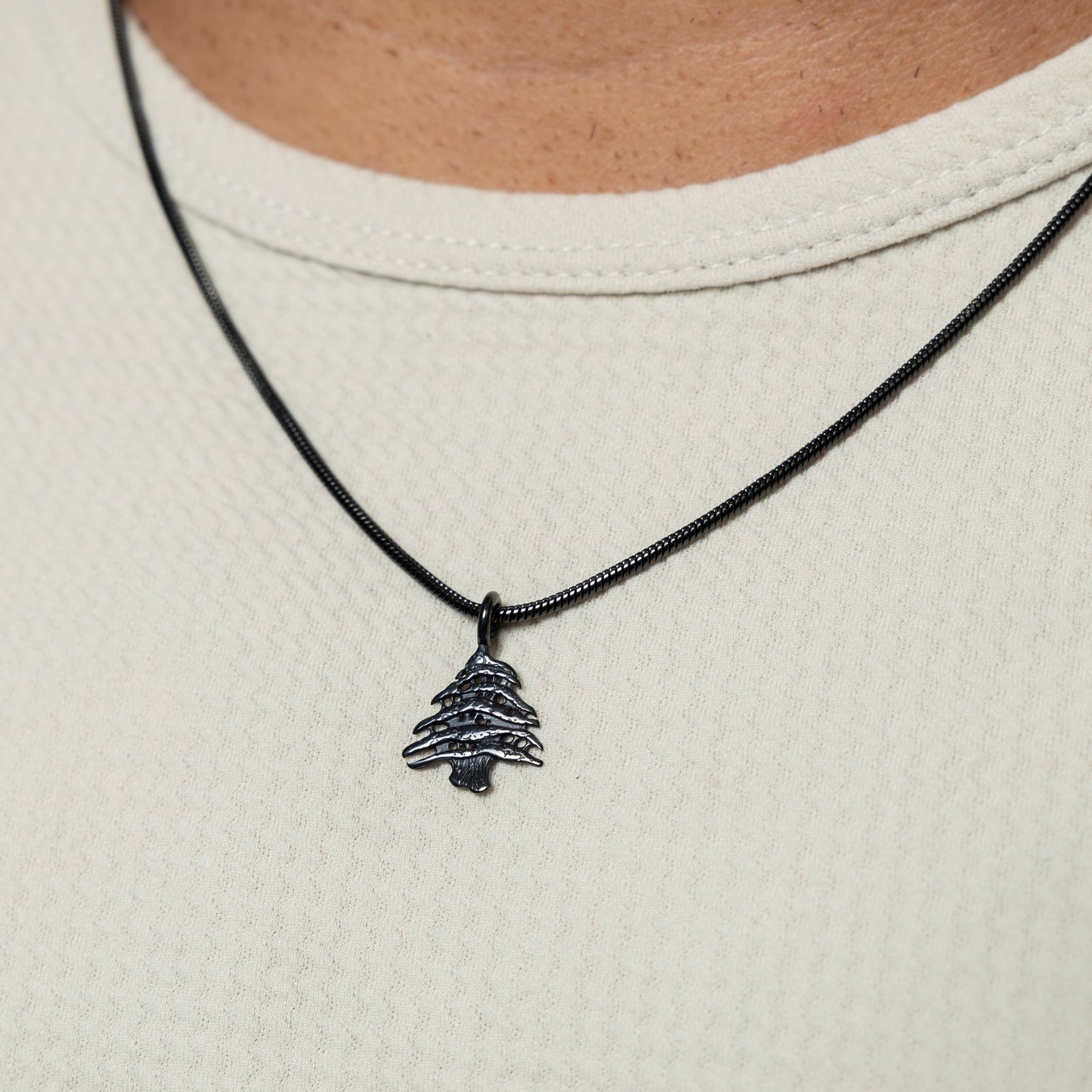 Close-up of a black Cedar of Lebanon necklace, worn over a white textured shirt.