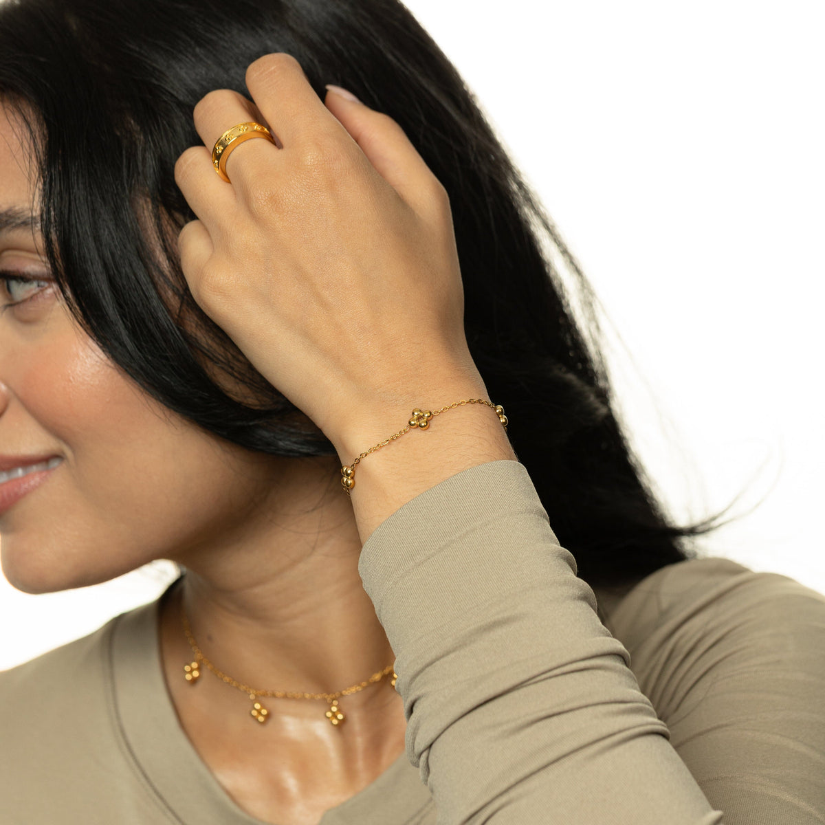 Woman wearing the gold henna bracelet with matching necklace and ring, hand raised to her hair.