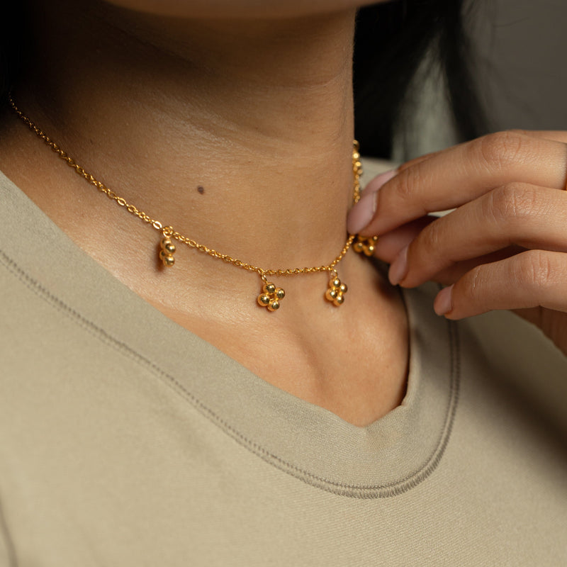 Close-up of the gold Henna Choker charms resting at the neckline pimage_ hand adjusting necklace.