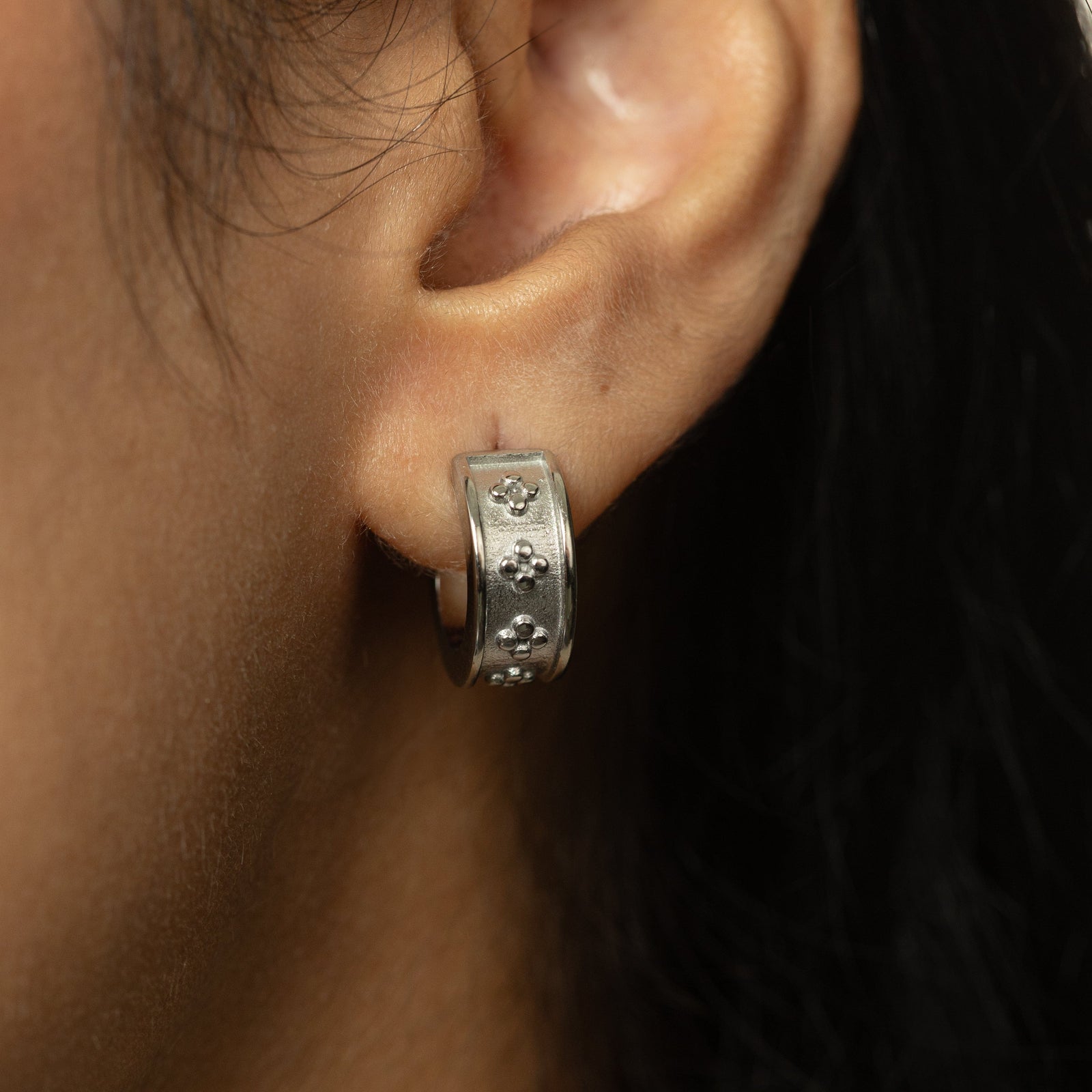 Close-up of silver Henna Hoop worn on ear, textured band with raised dotted floral details visible.