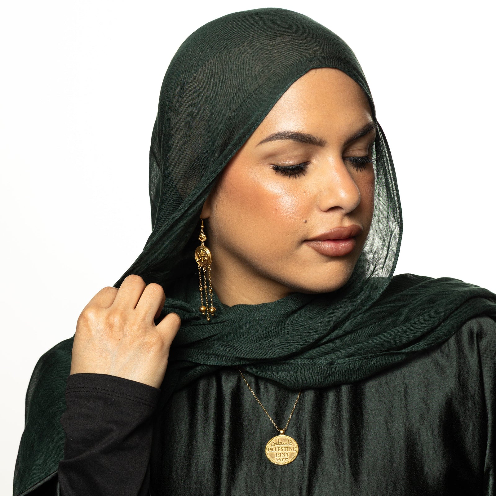 Model holds their hijab with their right hand. The model is wearing the gold Coin Mama Earrings.