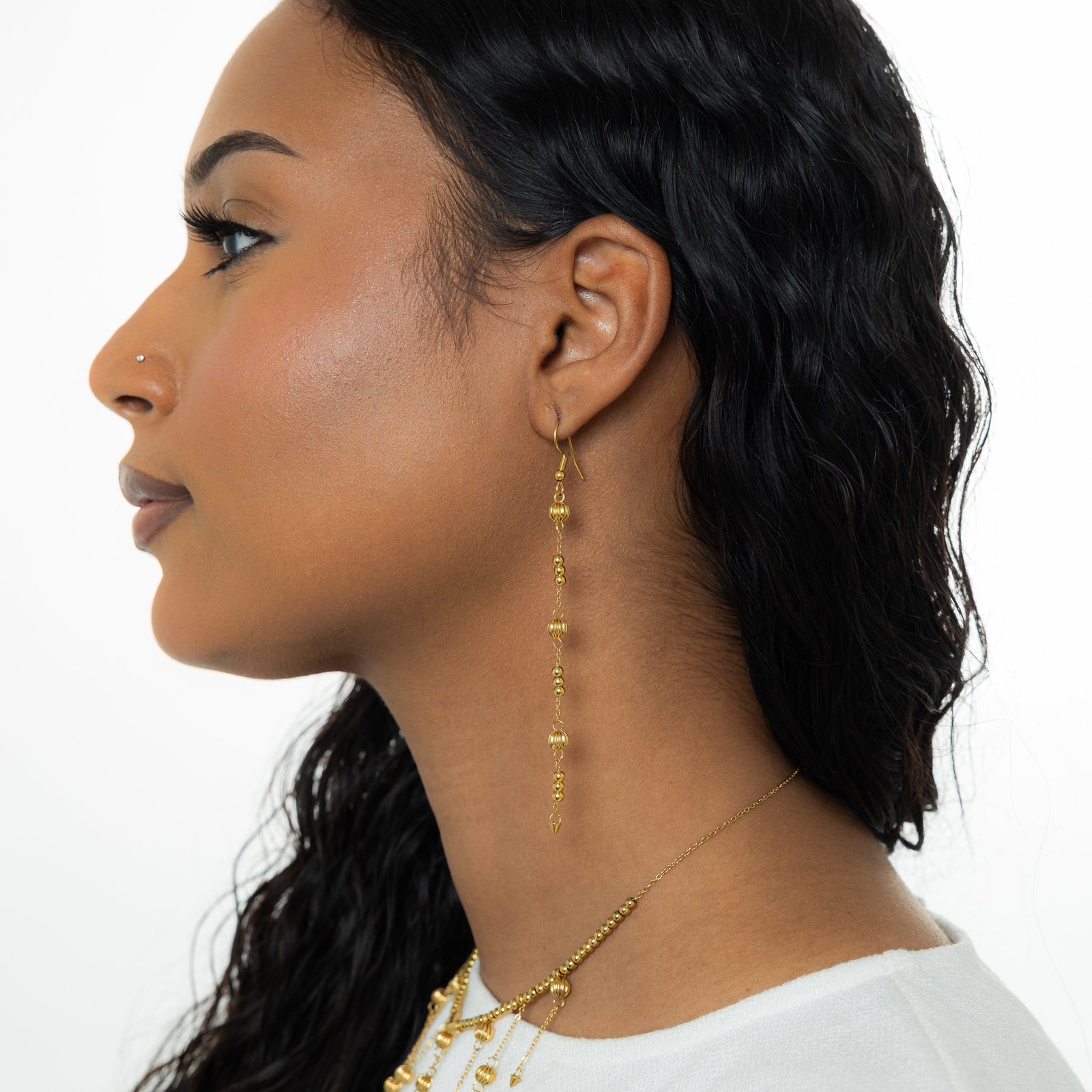 Photo of the left side profile of the model. The model is wearing the gold Comet Earring on their left ear.