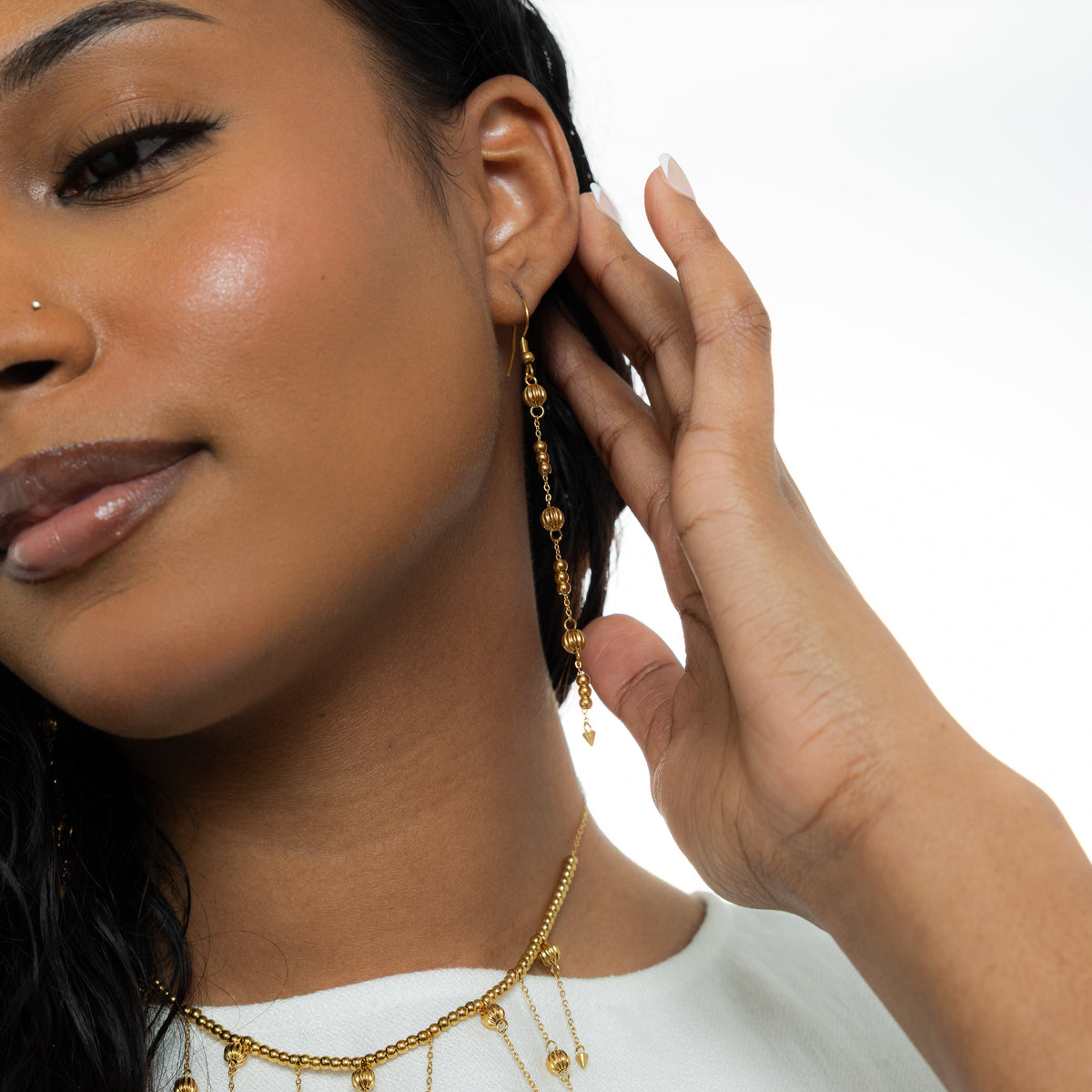 Photo of the model holding their hair behind their left ear. The model is wearing the gold comet earrings on their left ear.