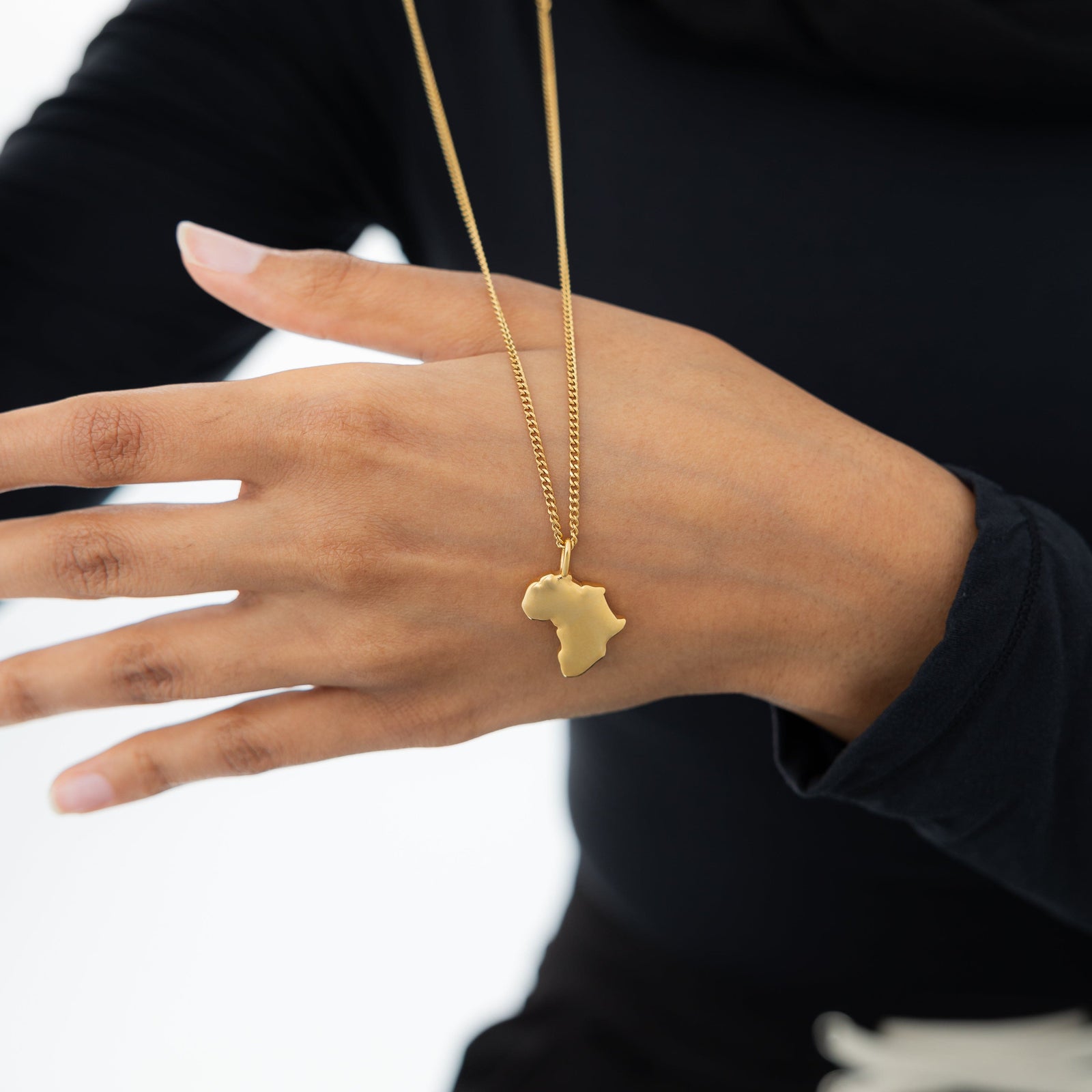 A model holding the chain of a gold-plated country map charm necklace, focusing on the fine craftsmanship of the charm and the delicate chain.
