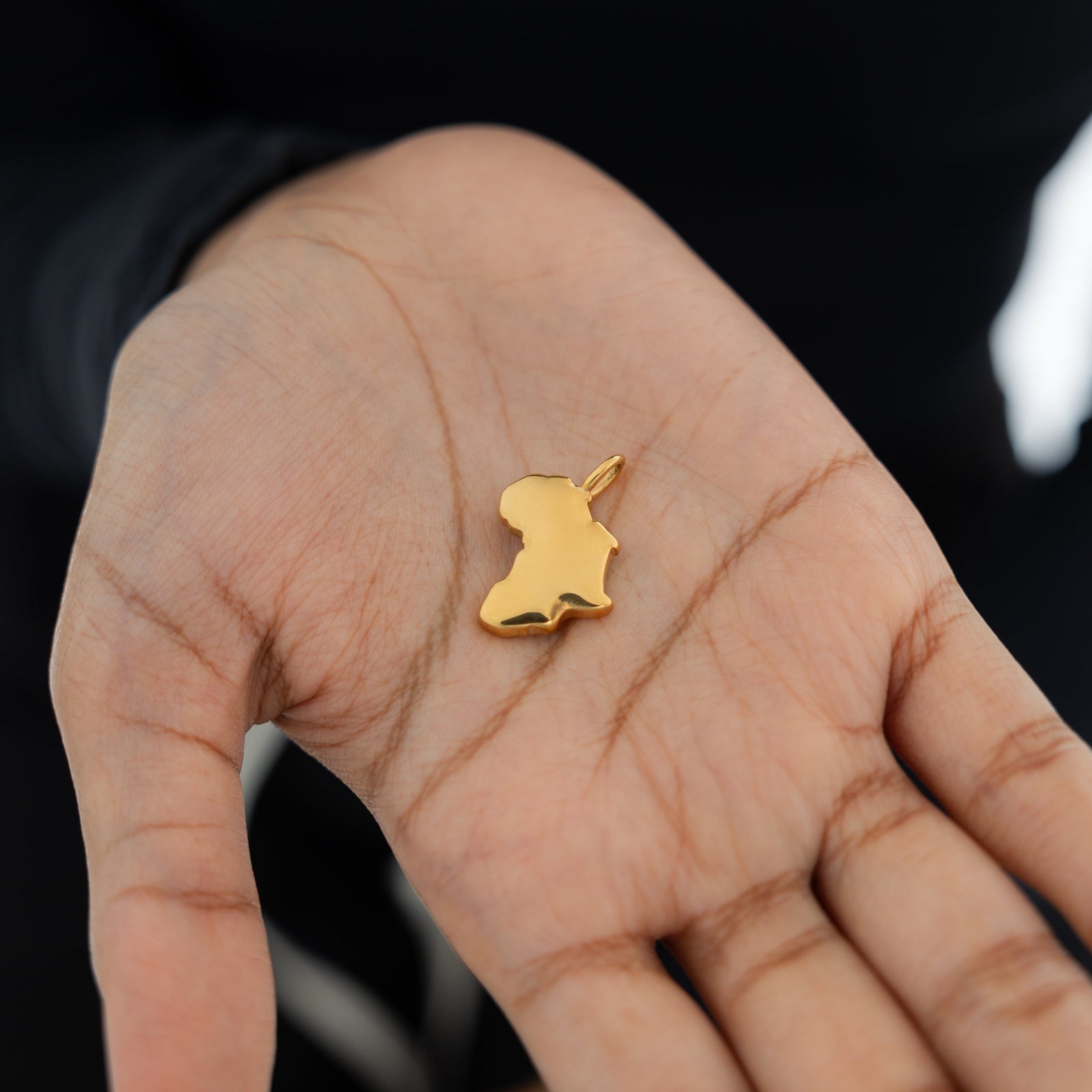 A model’s hand holding the chain of a gold-plated country map charm bracelet, emphasizing the charm’s fine craftsmanship and delicate design.