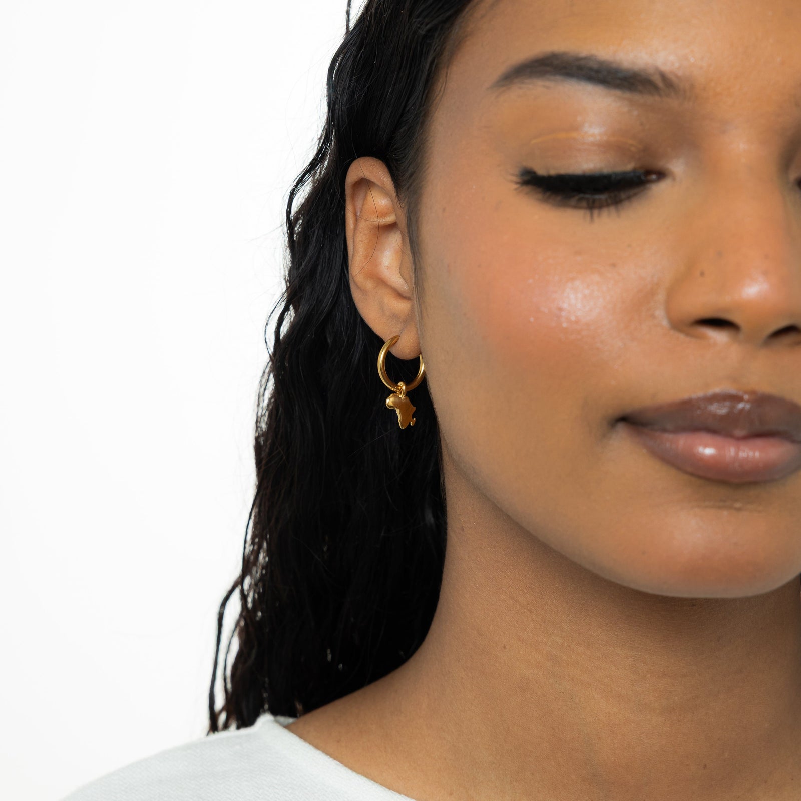 Photo of the right side of the model's face. The model is wearing the gold Country Map hoop.
