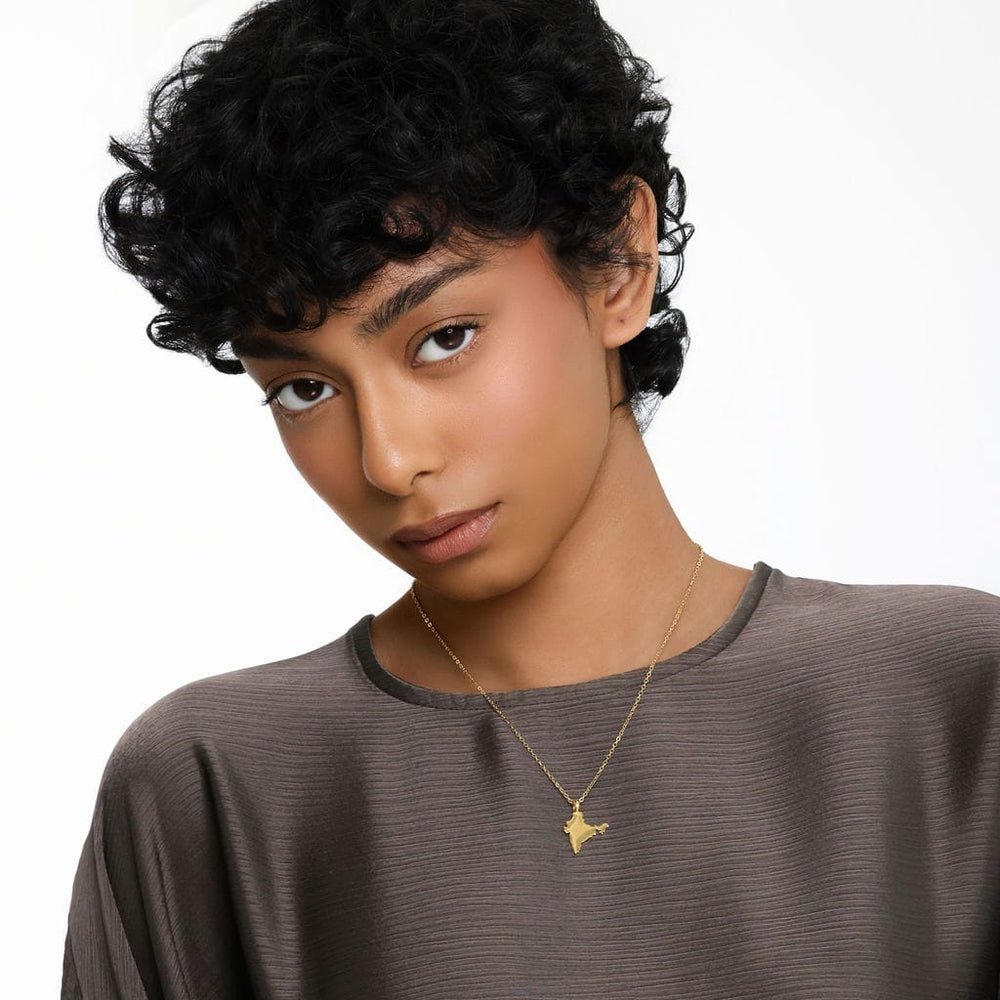 Photo of the model looking to the camera. The model is wearing the gold Country Map Necklace | Women.