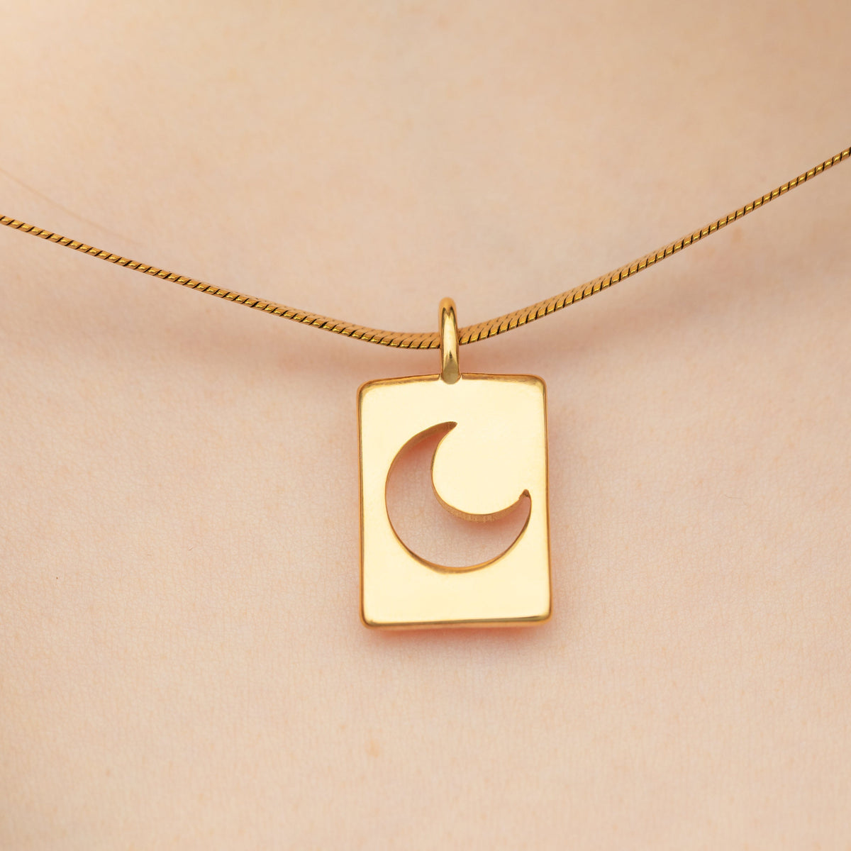 Crescent charm in gold worn on a thick chain, resting at the center of the chest on light skin.