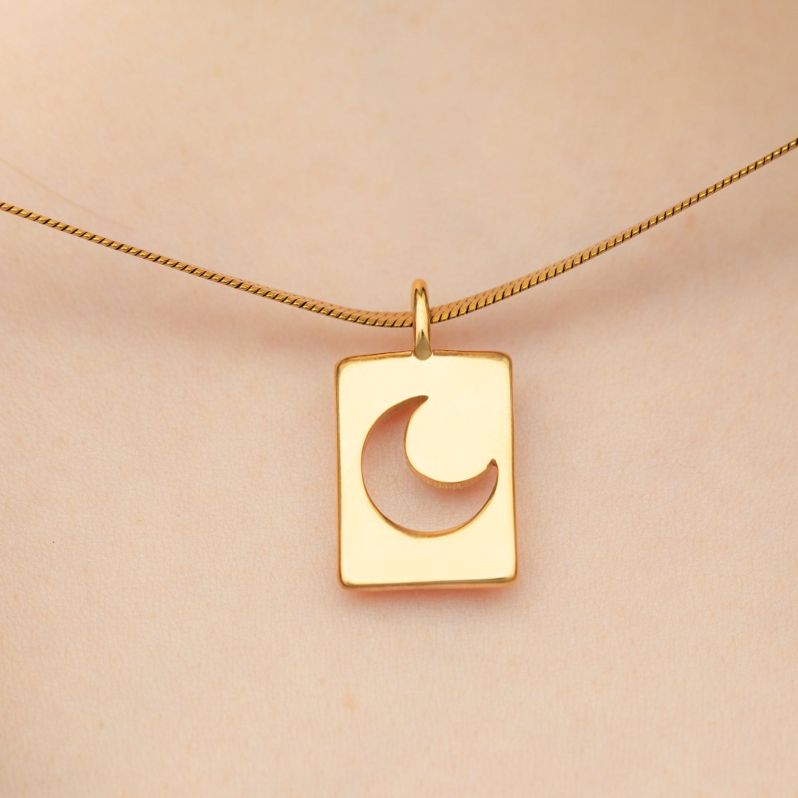 Crescent charm in gold worn on a thick chain, resting at the center of the chest on light skin.