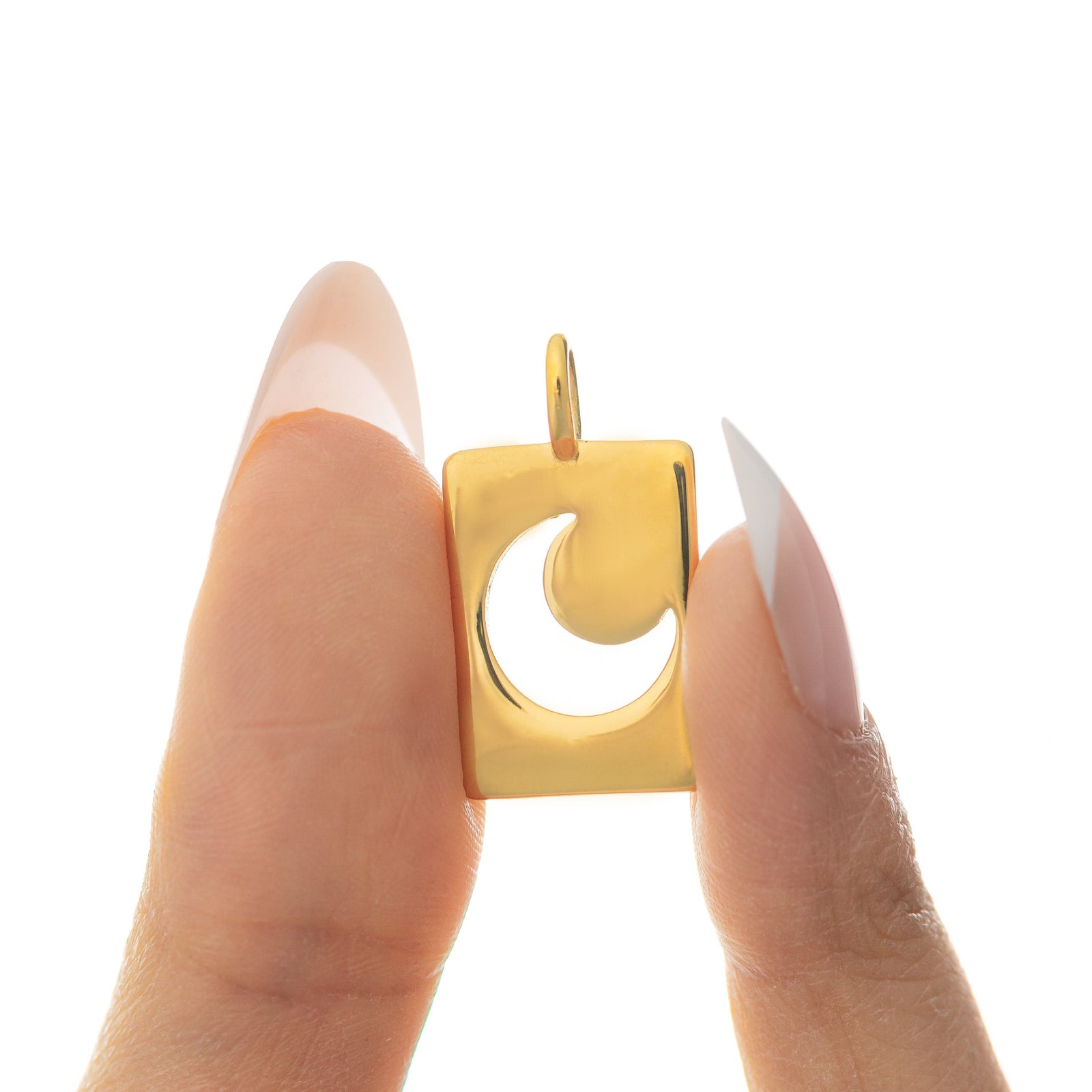 Gold crescent charm displayed between two fingers with long almond-shaped nails.