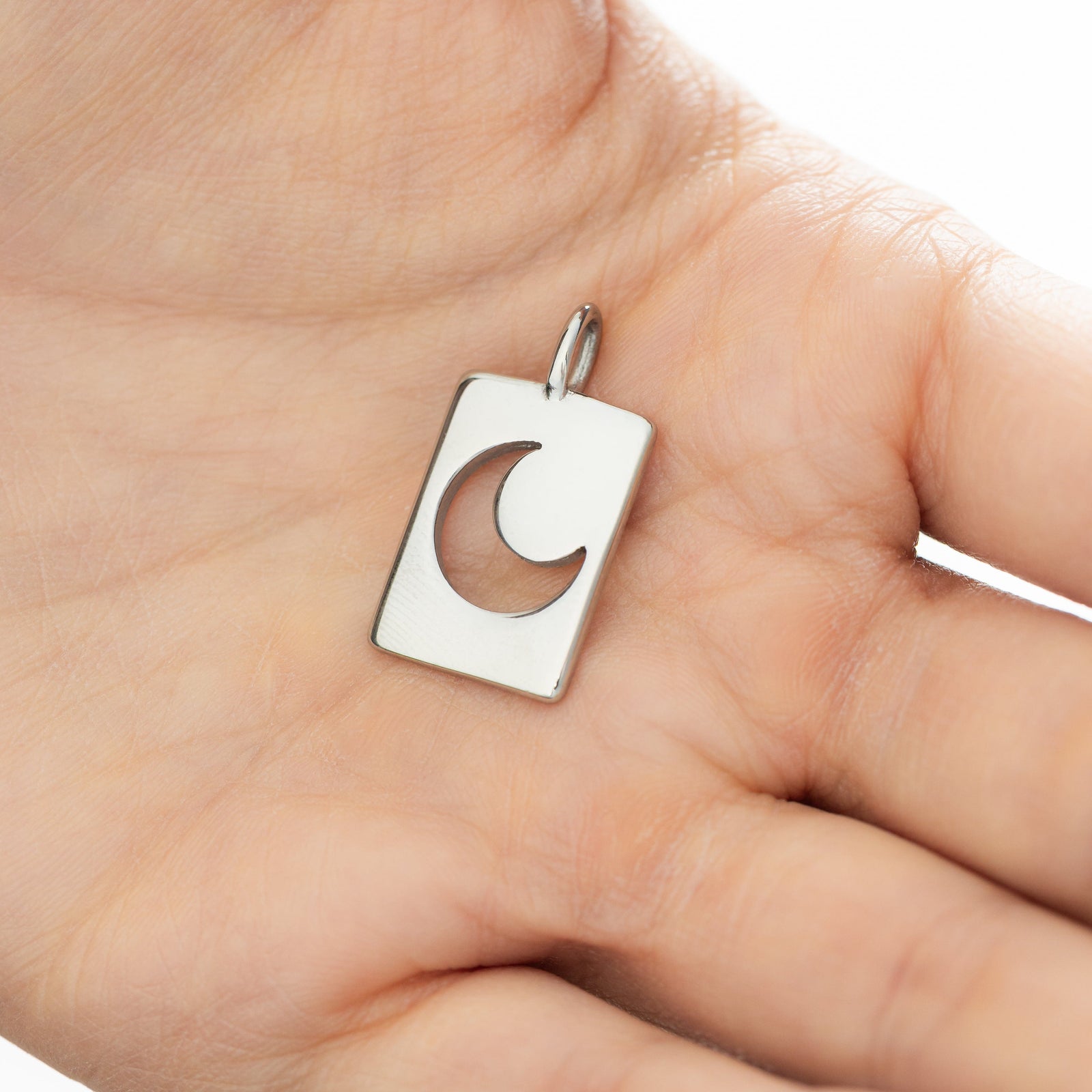 Silver crescent charm placed in an open palm, showing its cutout detail and smooth rectangular frame.