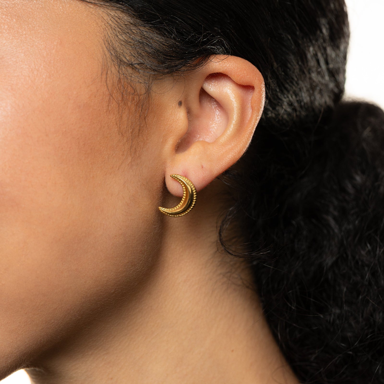 Close-up of an ear wearing a gold dotted crescent earring