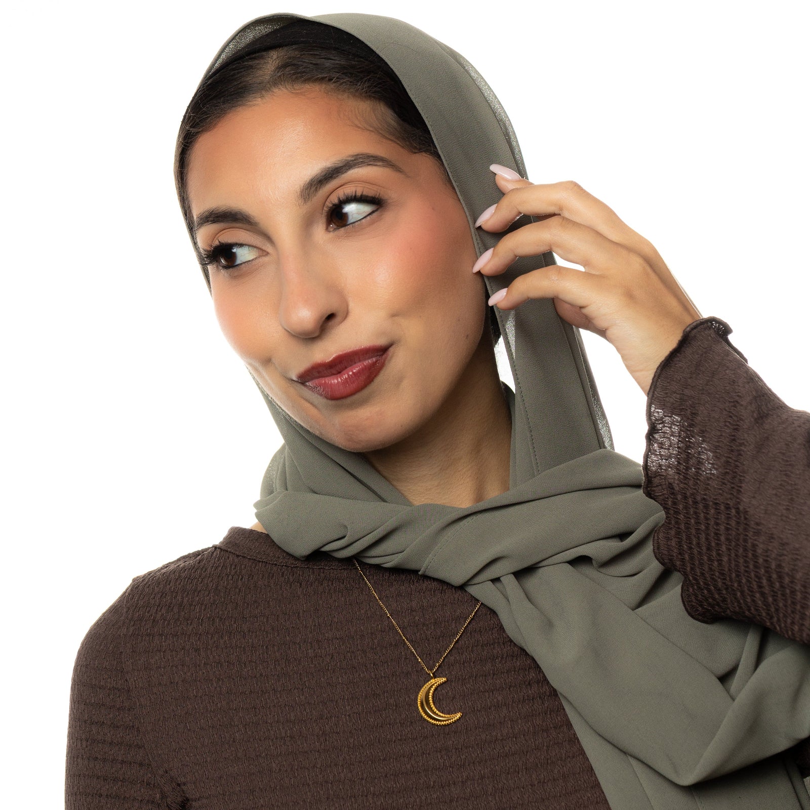Woman wearing a hijab and brown top with a gold dotted crescent necklace on a white background