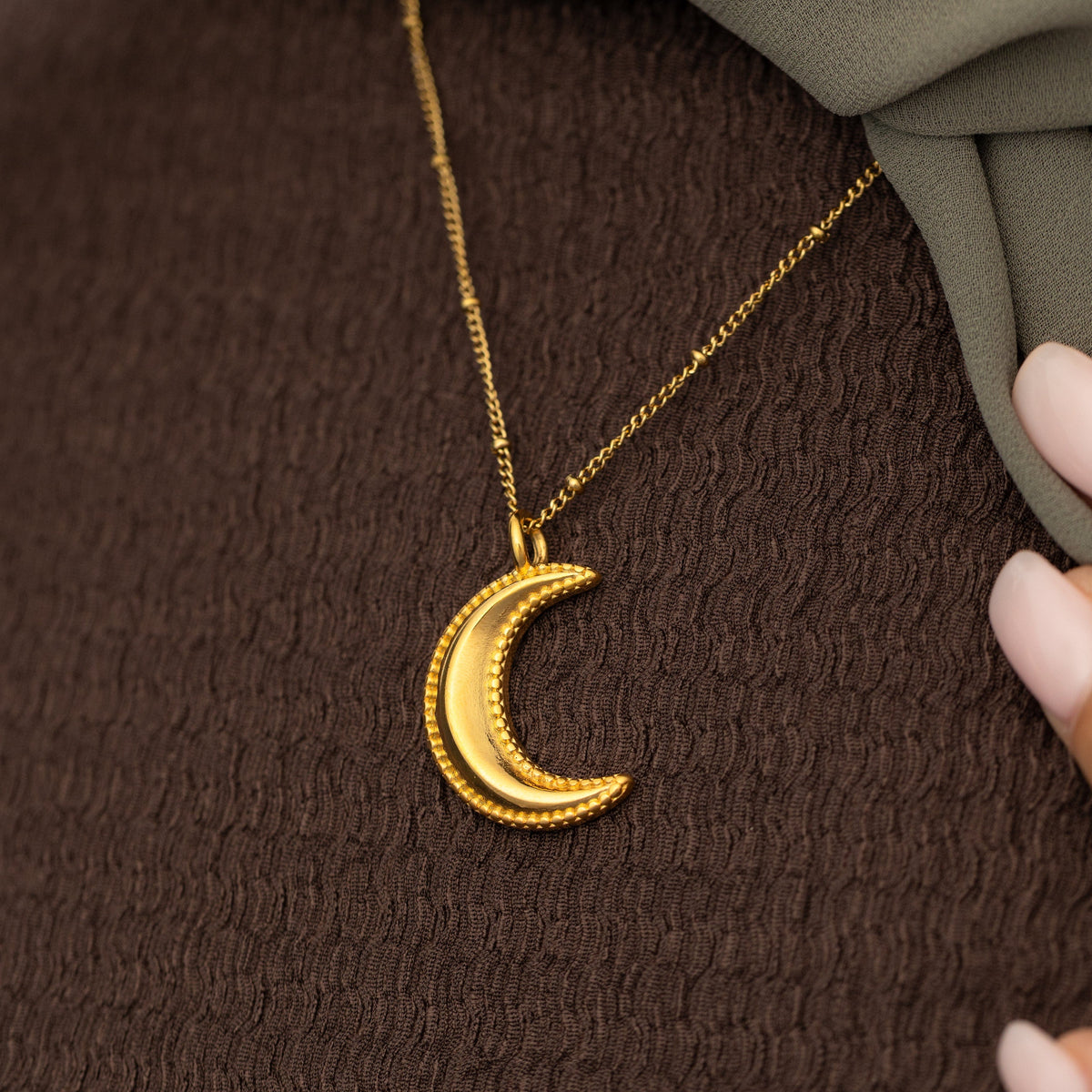 Gold dotted crescent necklace on a brown textured fabric background