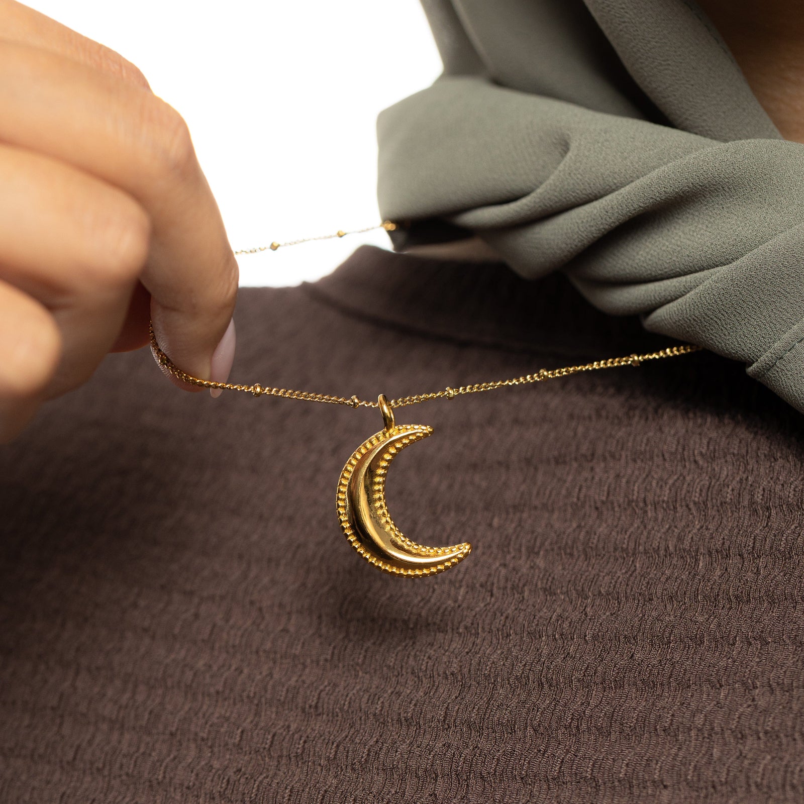 Gold dotted crescent necklace being held by a hand.