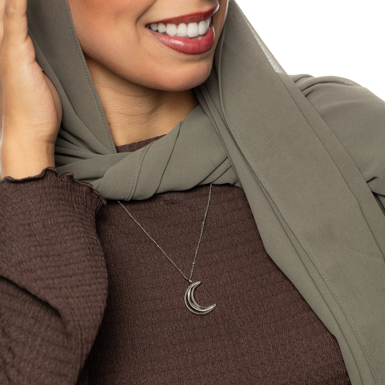 Woman wearing a brown top, a hijab, and a silver dotted crescent necklace..