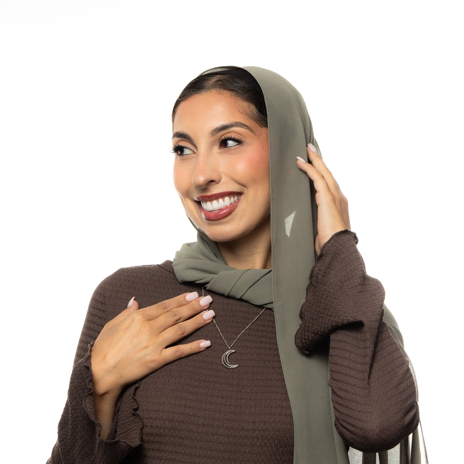 Woman wearing a brown top, a hijab, and a silver dotted crescent necklace.
