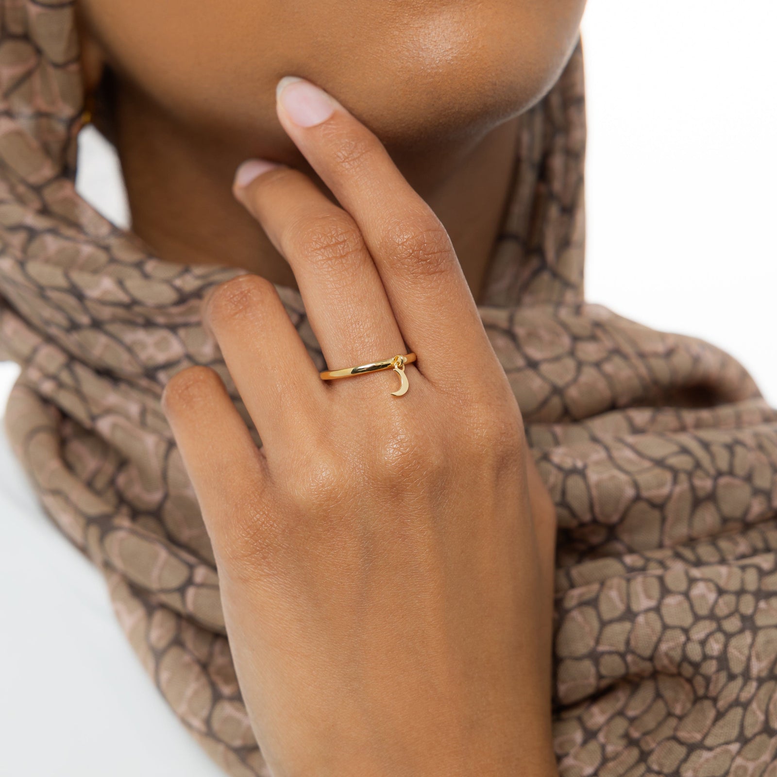Woman wearing a patterned beige hijab, hand posed near chin, showing the gold crescent ring.