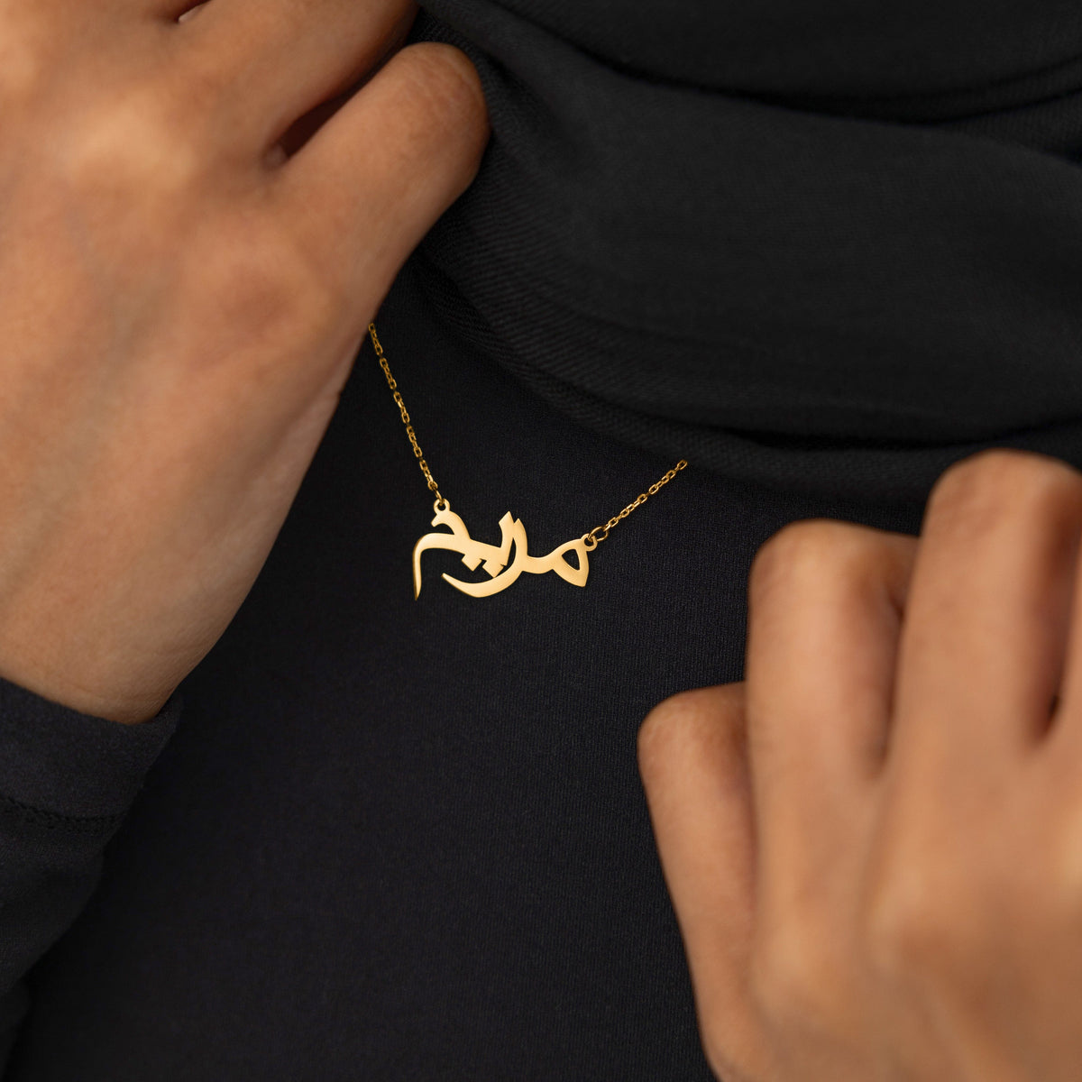 A model wearing the Custom Name Necklace in 14K solid gold at a 16-inch length. The necklace rests gracefully on the collarbone, showcasing the personalized Arabic name pendant against a simple, neutral-toned outfit.