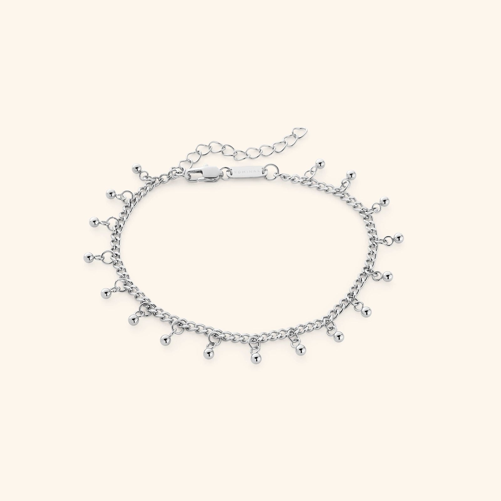 The Dangling Dotted Anklet in a polished silver finish. The anklet showcases a delicate curb chain with evenly spaced 3mm ball-shaped charms that dangle, offering a minimalist and elegant aesthetic.
