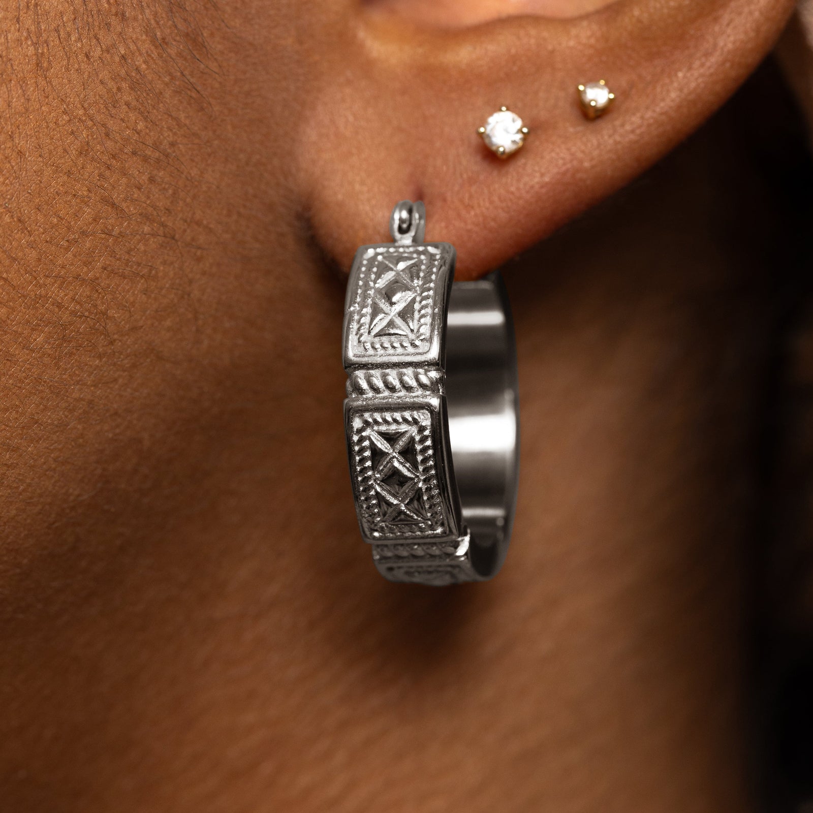 Photo of the model's left ear. The model is wearing a couple of earrings in different parts of their ear, one of which is the silver Damascus Tile Earrings
