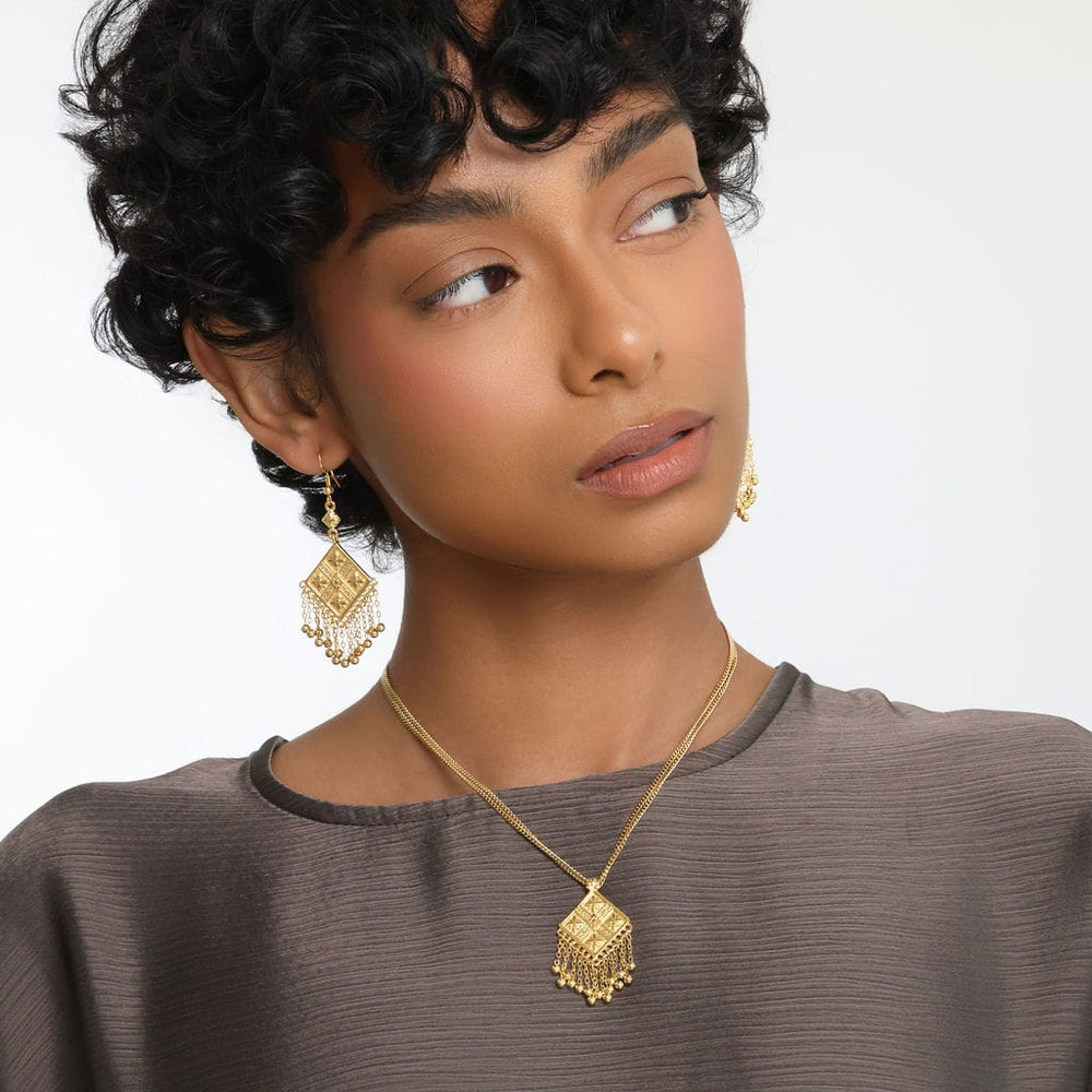 Photo of the model looking away from the camera. The model is wearing a pair of gold dangling earrings and gold Dancing Kite Necklace.