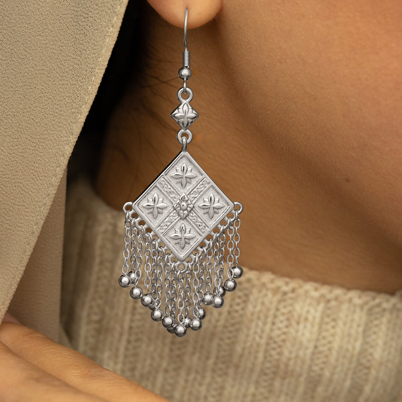 Silver Dancing Kite Earring with an engraved square design and hanging chains worn on a woman's ear in a close-up shot.