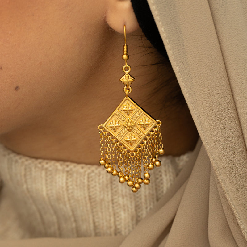 Gold Dancing Kite Earring with an engraved square design and hanging chains worn on a woman's ear in a close-up shot.