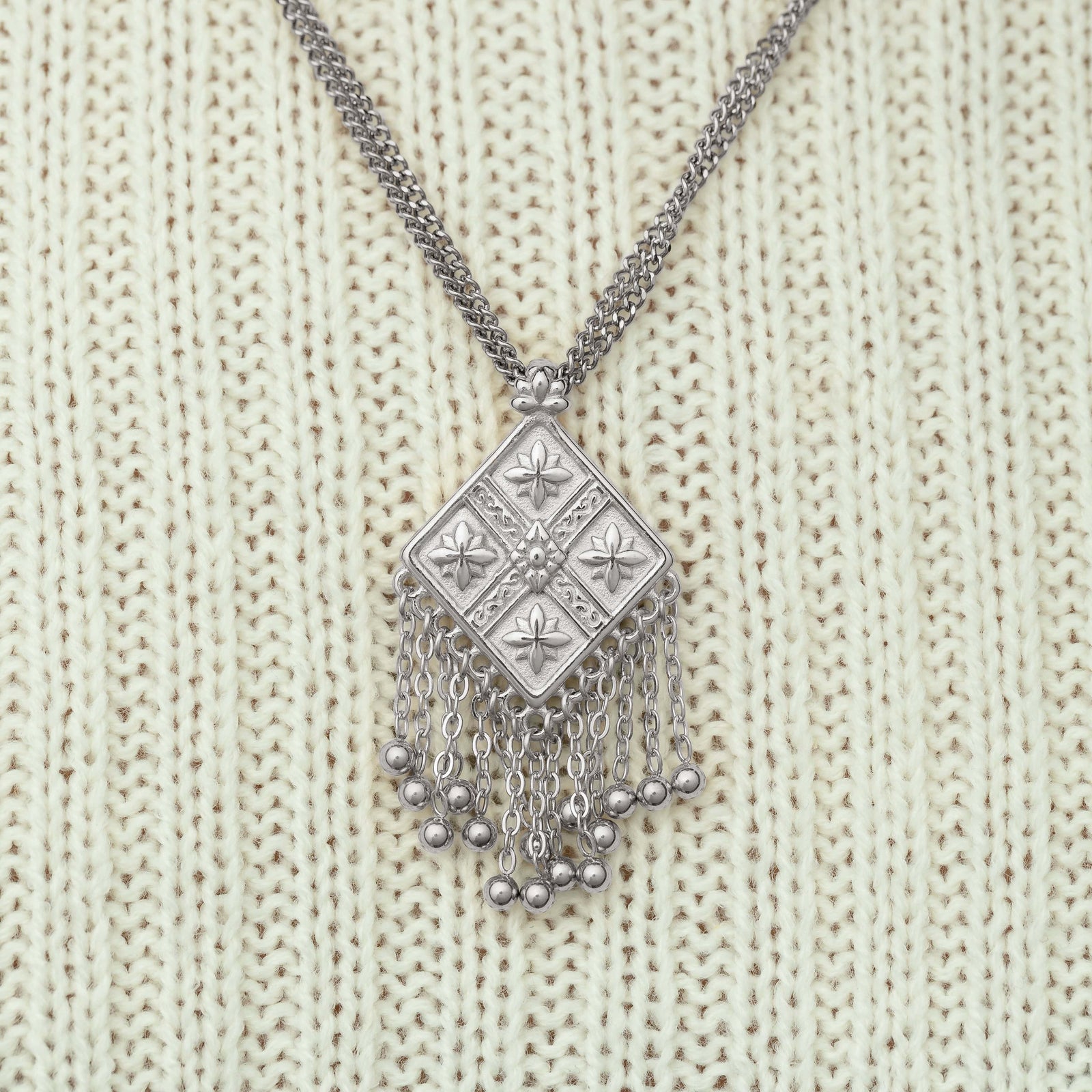 Close-up of a silver dancing kite necklace, styled against a cream ribbed sweater.