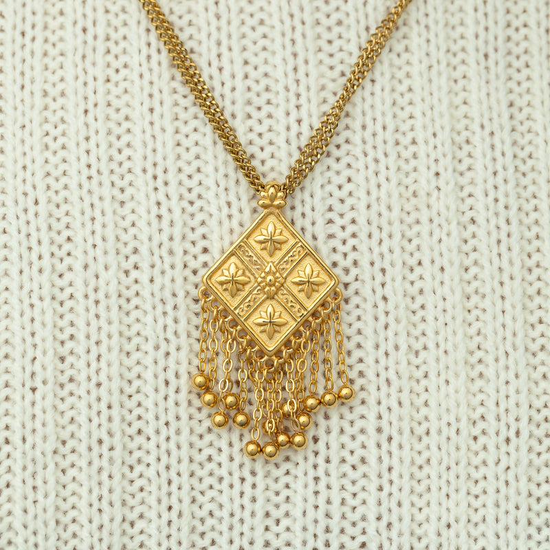 Close-up of a gold dancing kite necklace pimage_ styled against a cream ribbed sweater.