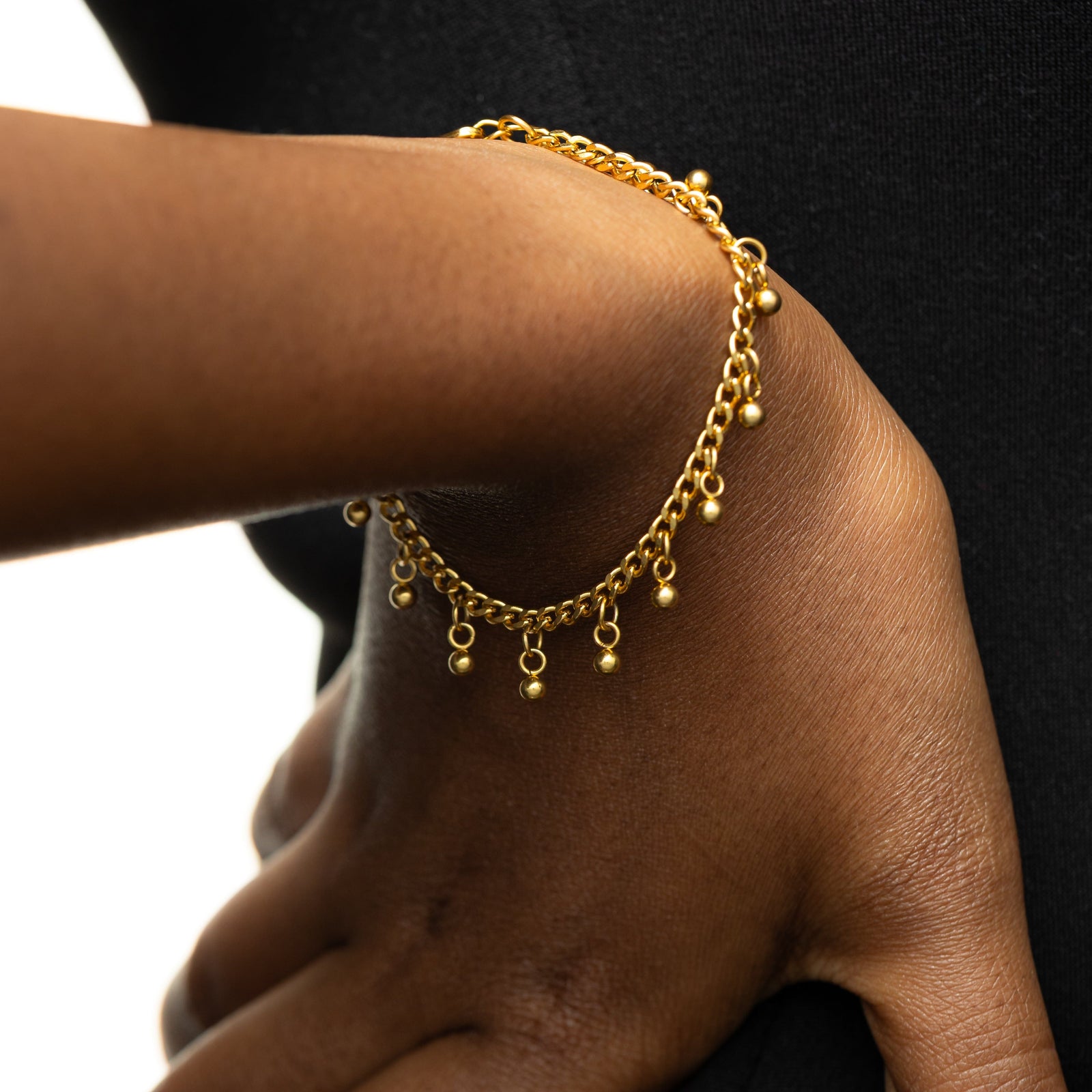 Gold Dangling Dotted Bracelet worn by a model on their right hand.