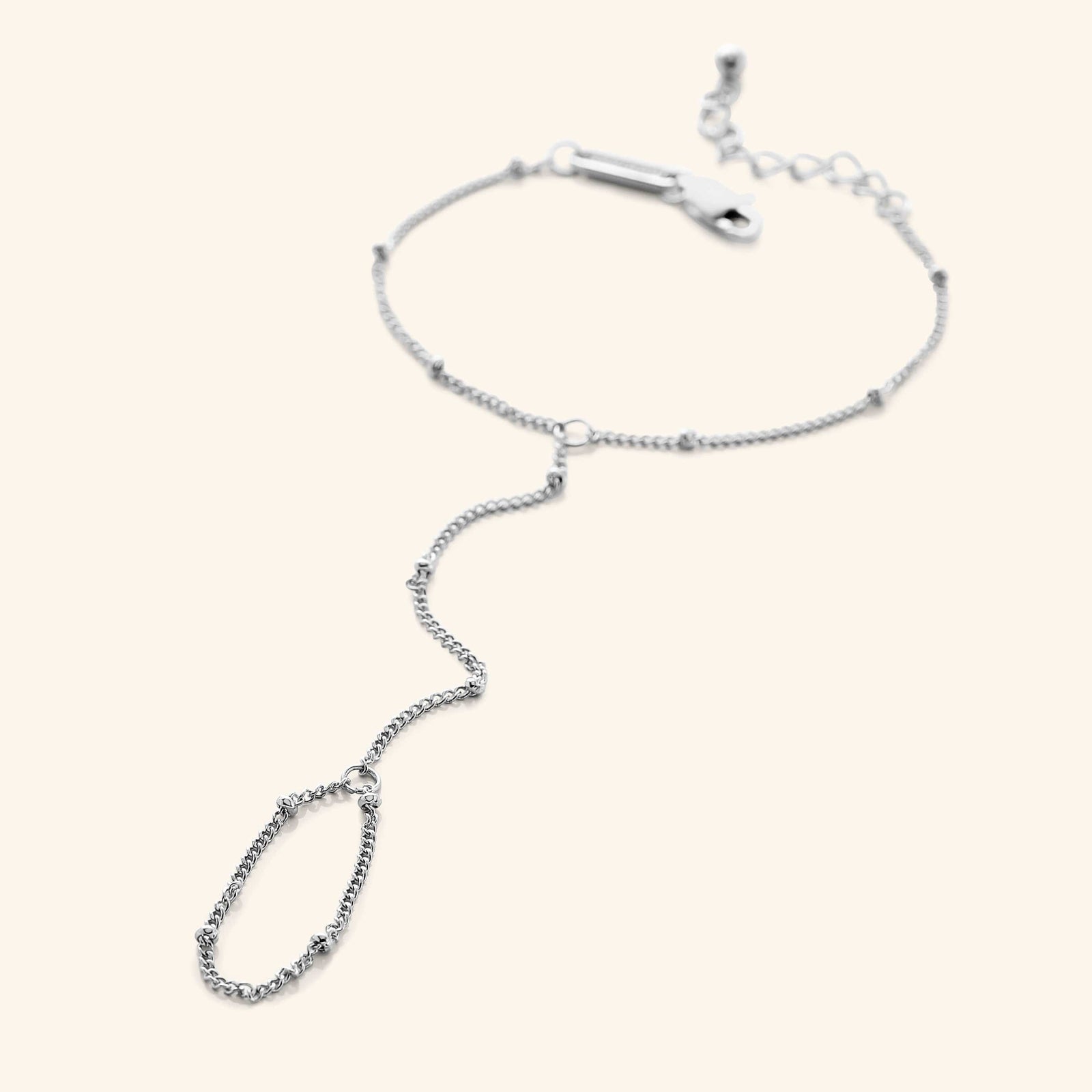Flat lay of a  silver dotted hand chain with a slim bracelet attached to a matching finger loop by a fine chain.