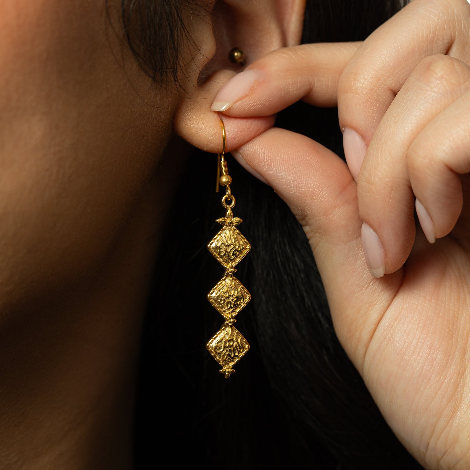 Close up photo of the gold Draping Thikr Earrings as worn by the model.