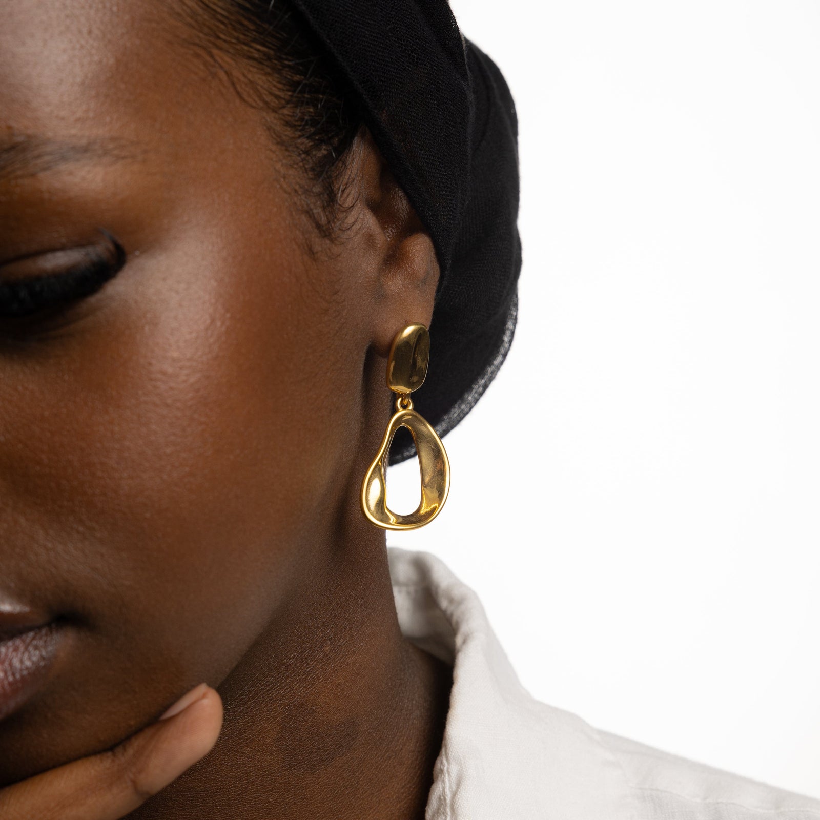 Close up of the left side of the model's face. The model is wearing the gold Droop Earring on their left ear.