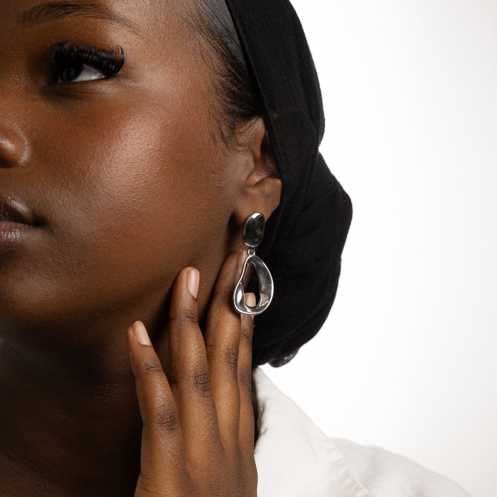 Close up of the silver Droop Earrings as worn by the model on their left ear.