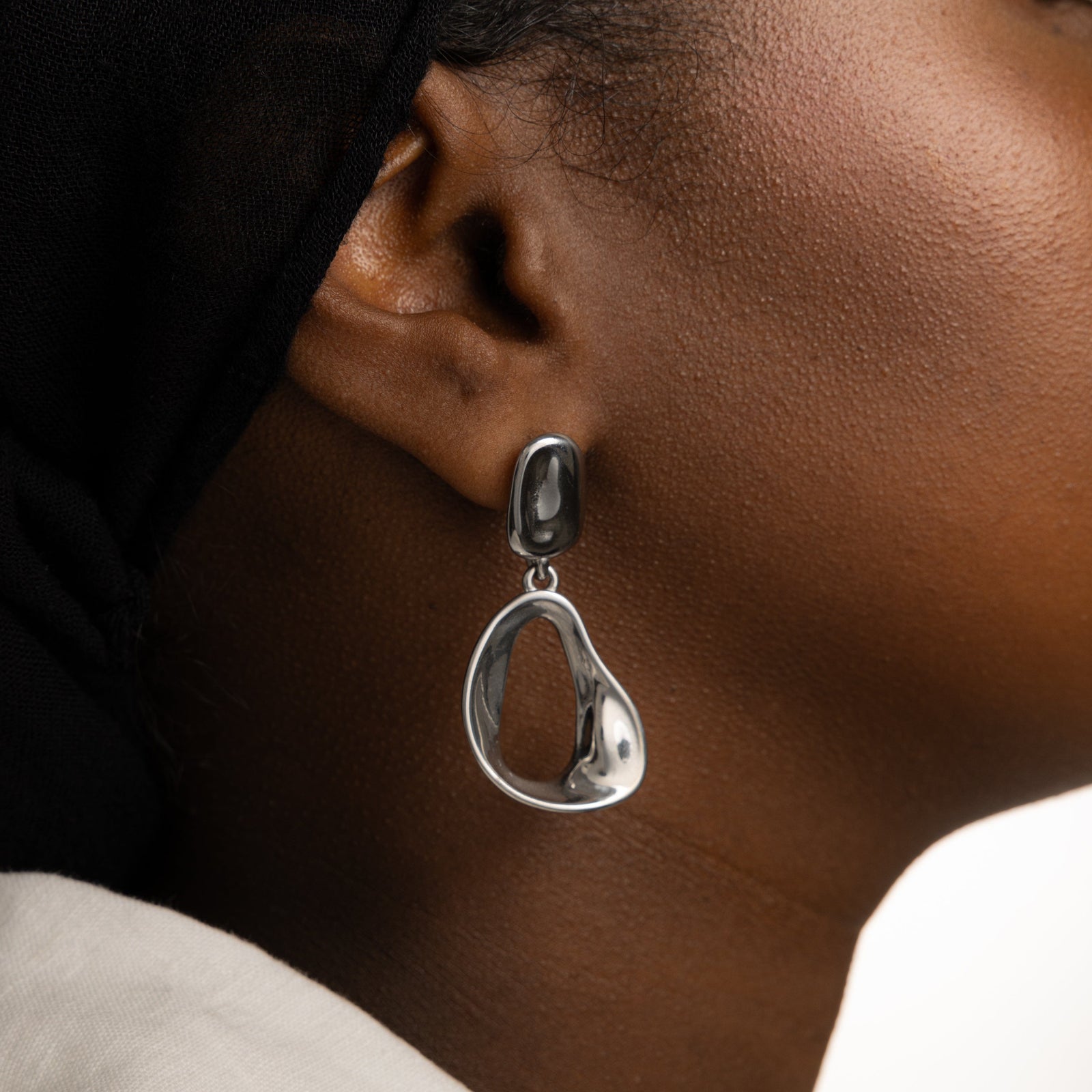 Close up of the silver Droop Earrings as worn by the model on their right ear.