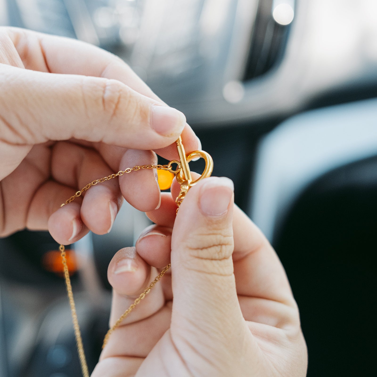 Close-up of hands fastening the toggle clasp of the gold Duaa Al-Safar chain.