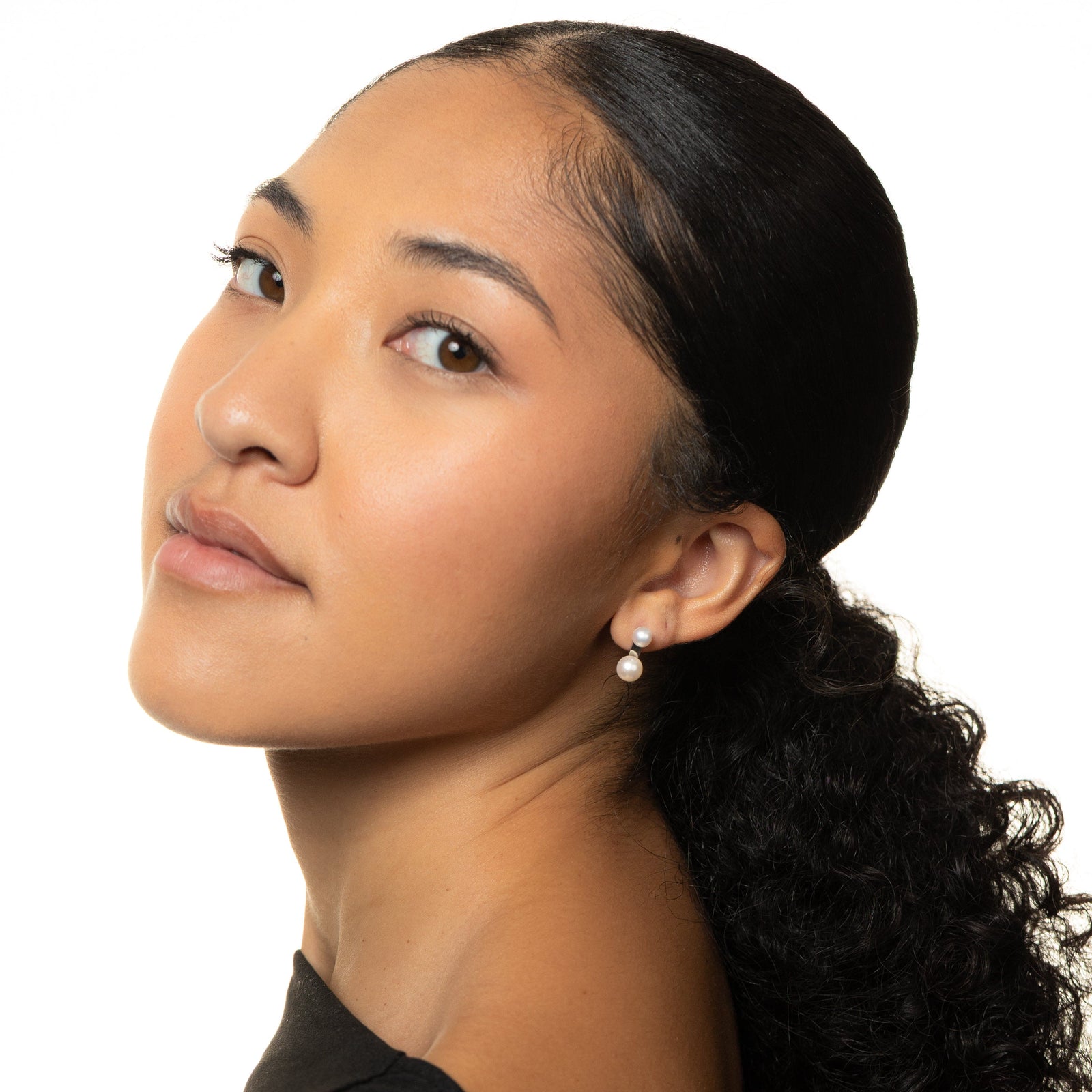 Woman with a ponytail wearing a gold duo pearl stud, shot on a white background