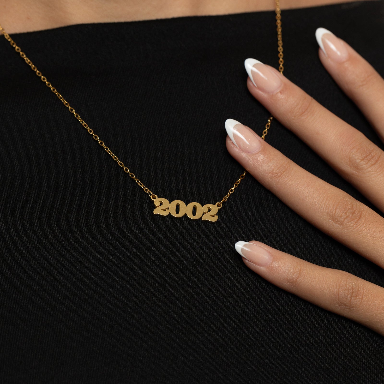 Gold English Birthyear necklace with '2002' pendant, a hand slightly touching the chain.